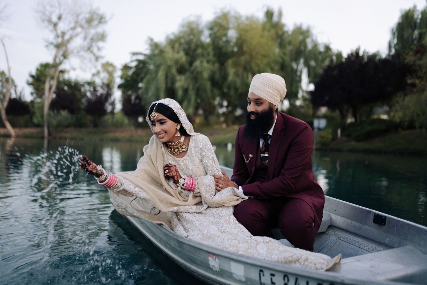 A playful couple splashes water while sitting in a rowboat on a calm lake.