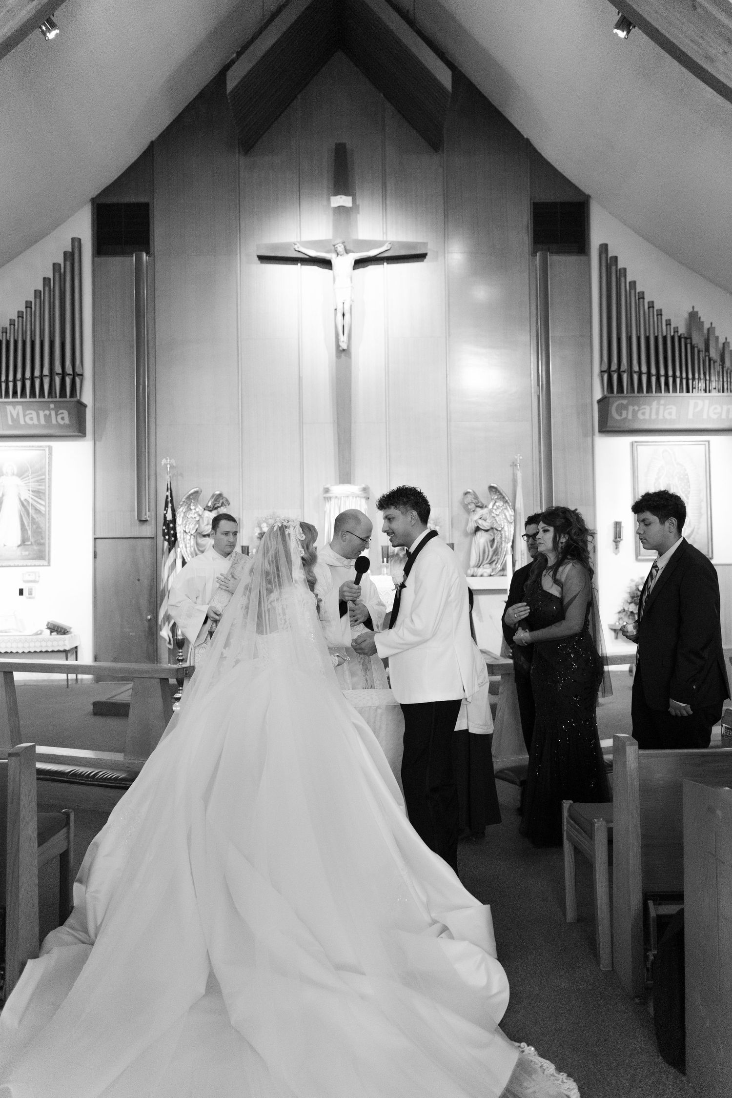 A black and white photograph of a wedding ceremony beneath a large crucifix in a church.