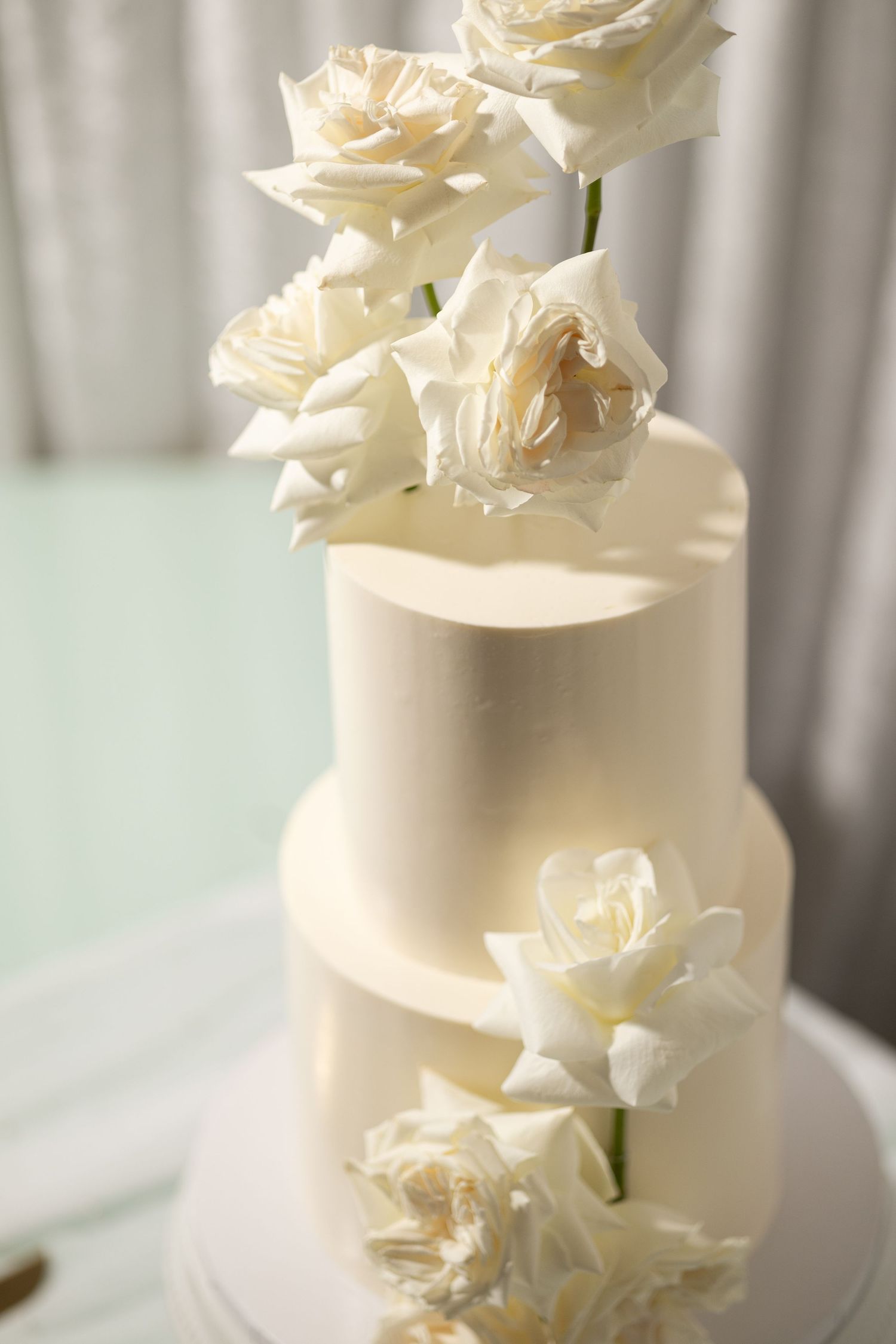 Close-up of a white wedding cake decorated with cream-colored roses against a light background.