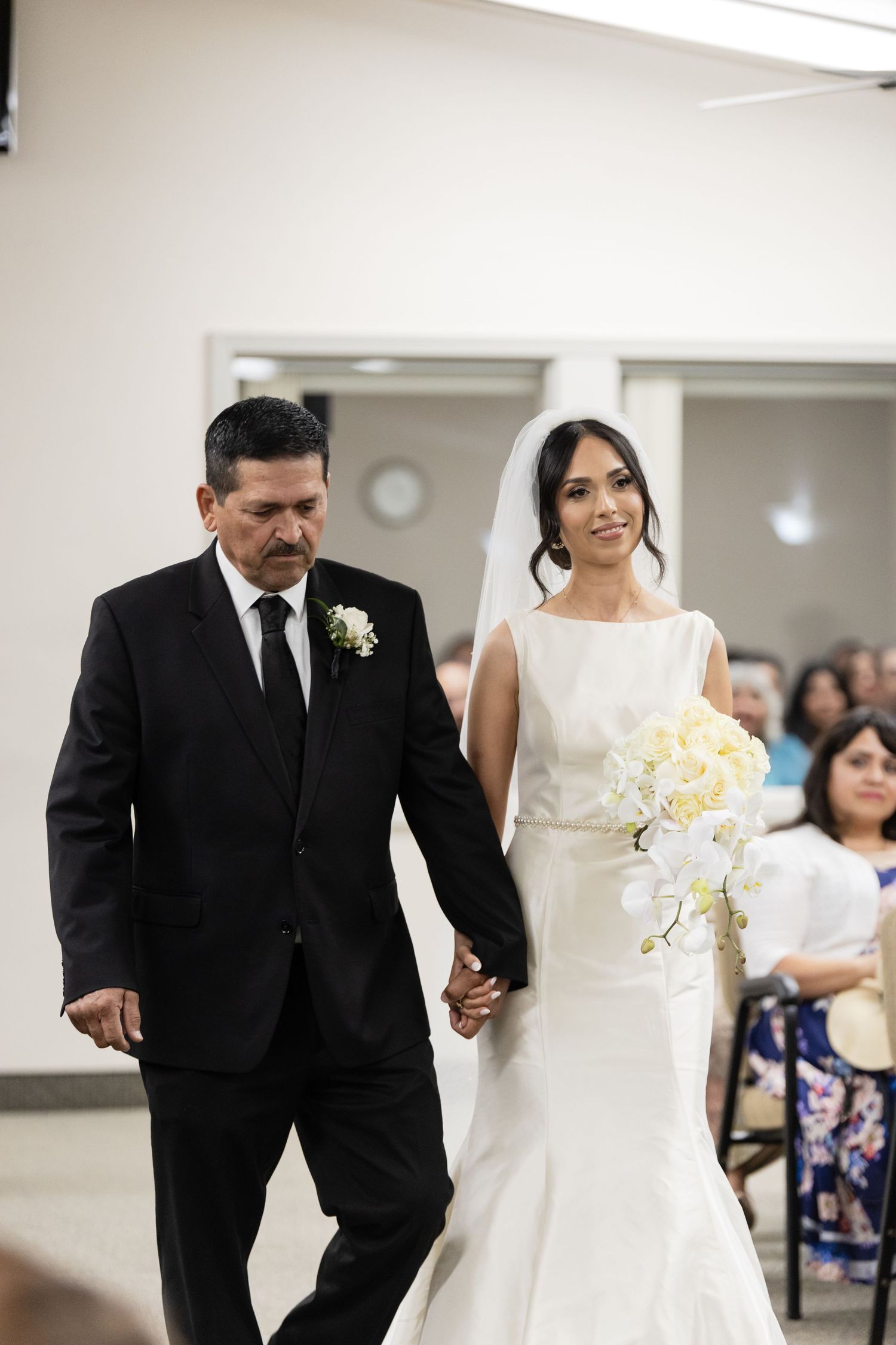 Wedding ceremony processional in bright indoor venue with bride in white dress walking down aisle.