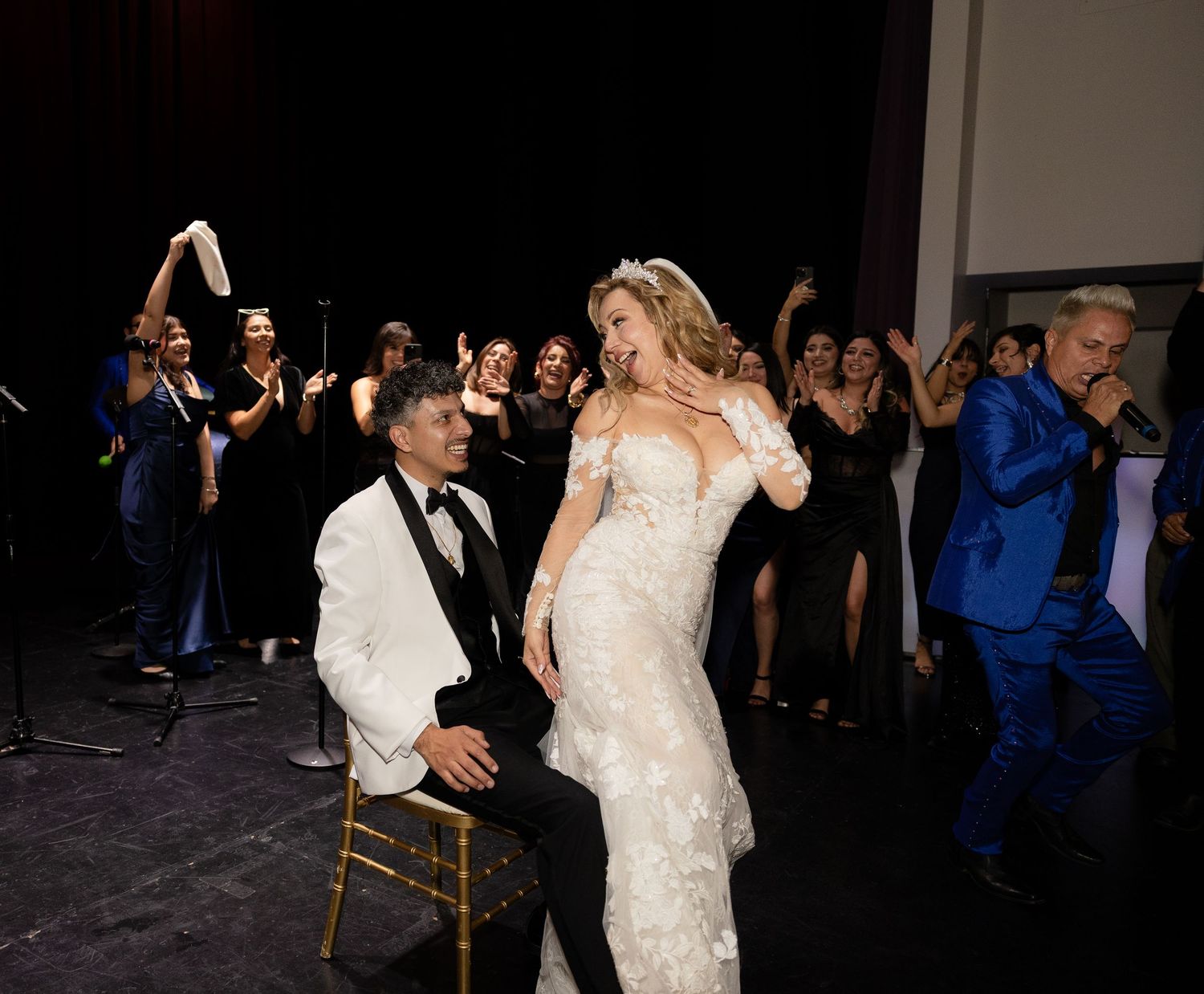 A couple shares a romantic moment during their wedding reception as guests dance in the background.