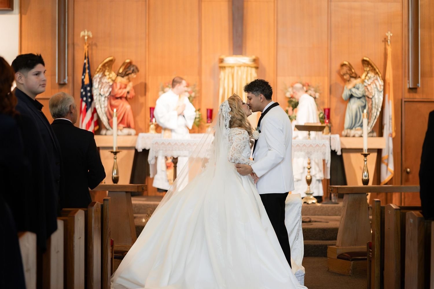 A wedding ceremony captured in warm lighting with decorative angel statues flanking the altar.