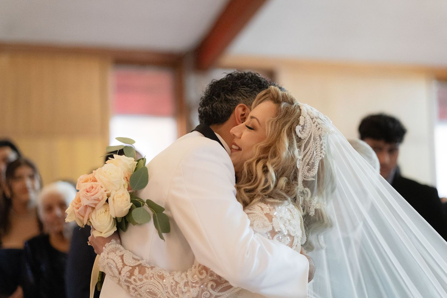 Bride in an elegant white lace wedding gown with a long veil during a church ceremony.