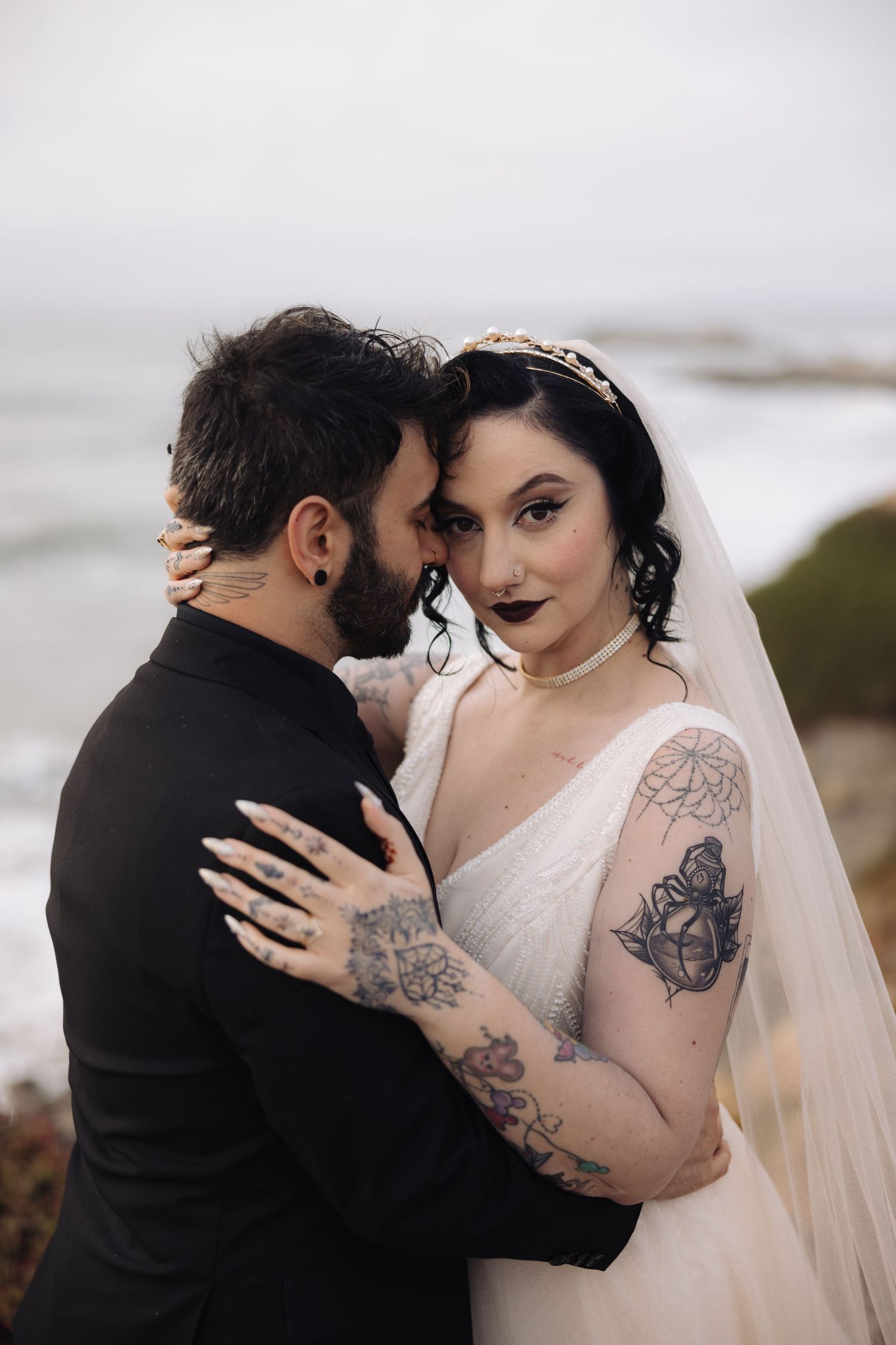 An elegant gothic-styled wedding portrait captured against a moody coastal backdrop.