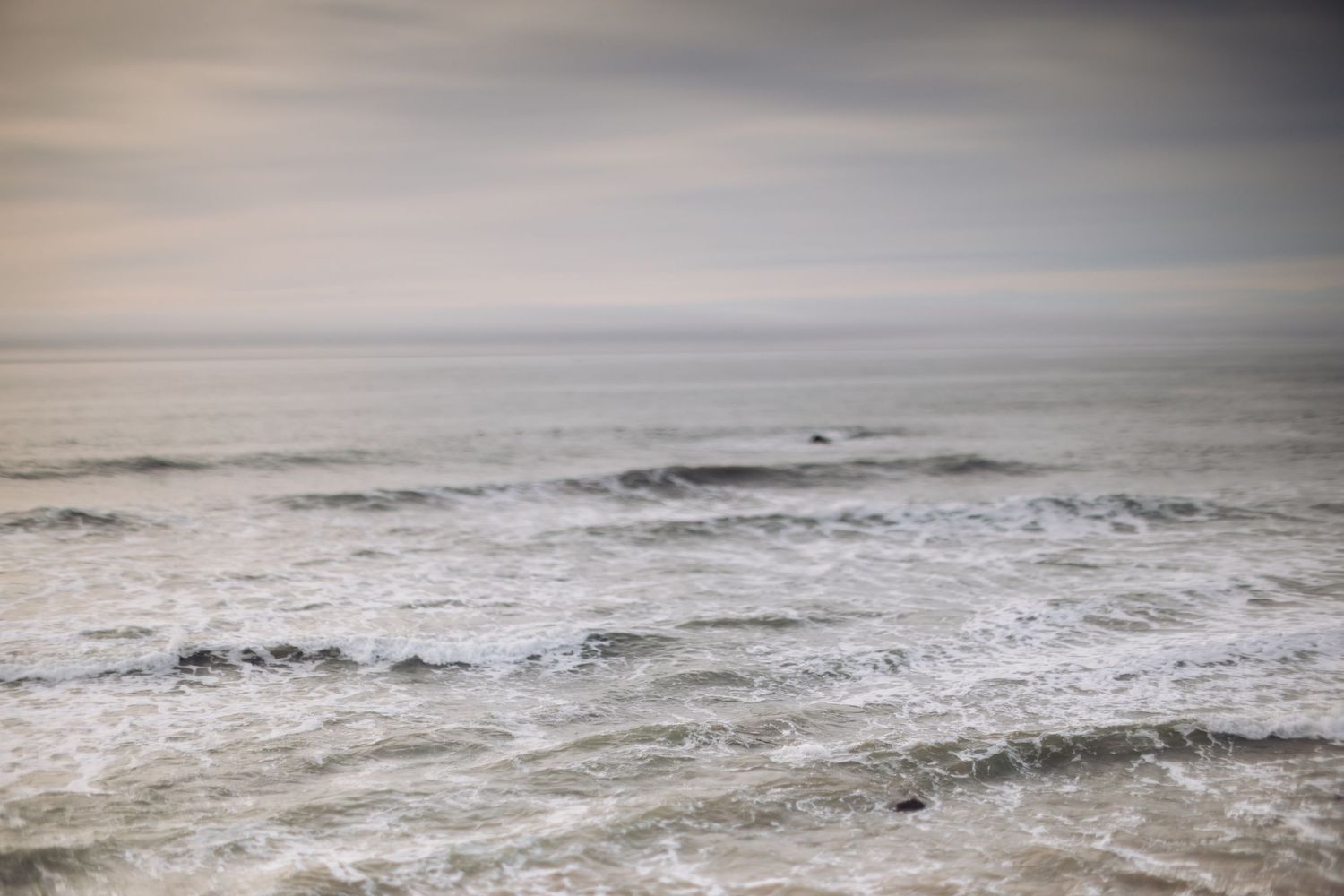 Dramatic waves crash against a rocky coastline under an overcast sky.