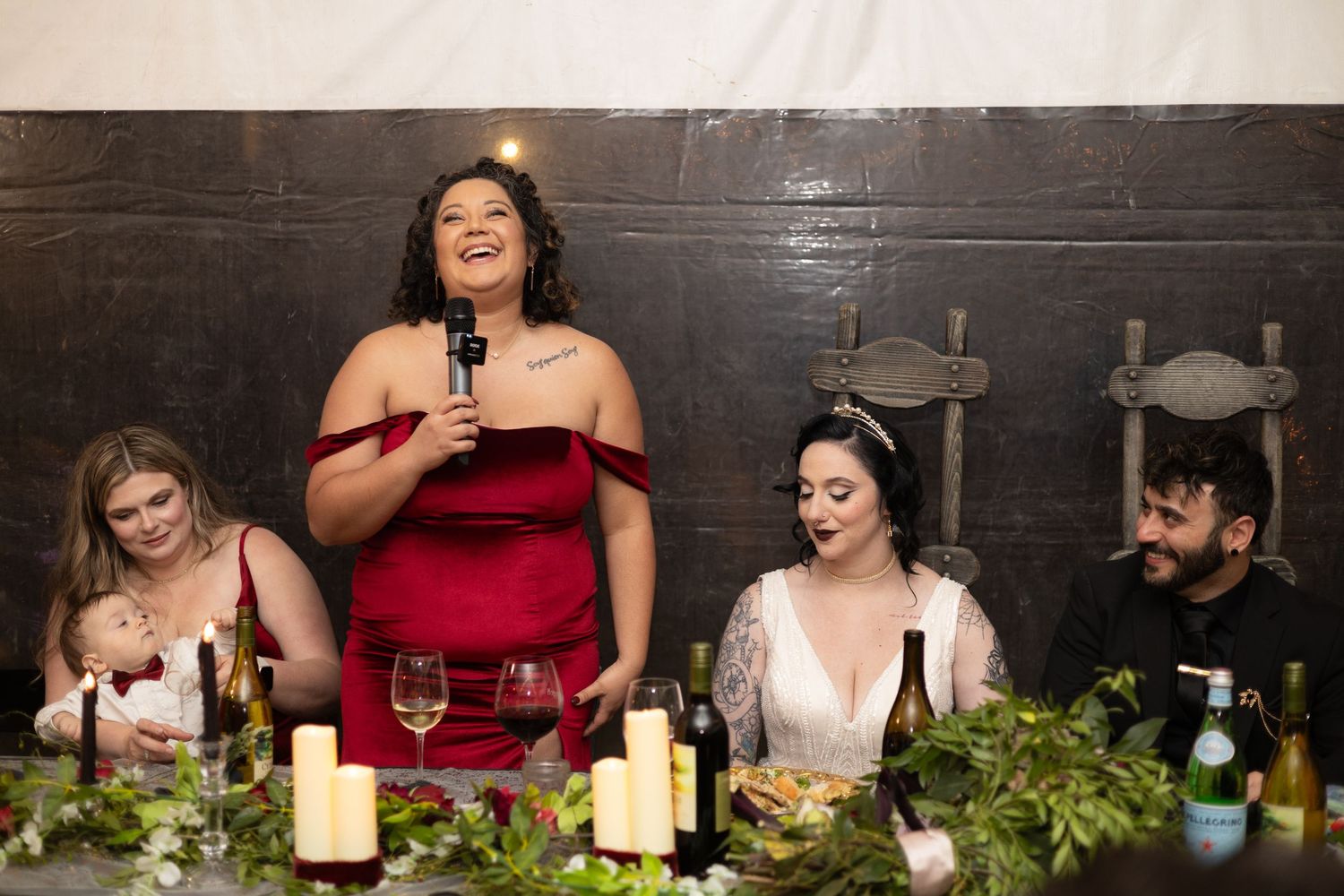 Wedding guests share laughter and conversation around an elegantly decorated dinner table with candles and greenery.