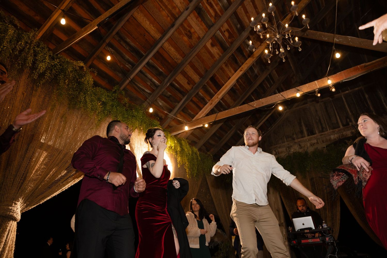 Partygoers dancing enthusiastically beneath string lights in a rustic barn setting.