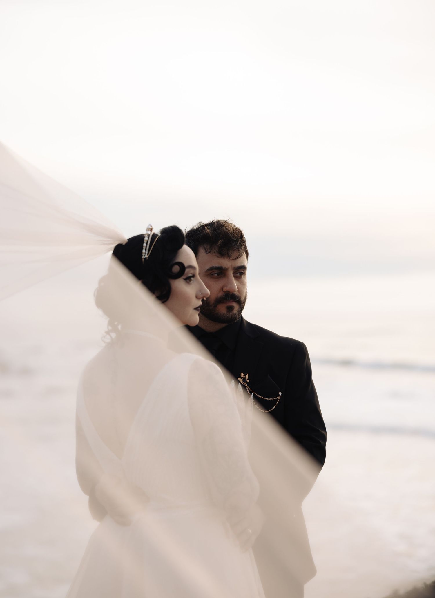 Romantic coastal wedding scene with billowing white veil catching the ocean breeze.