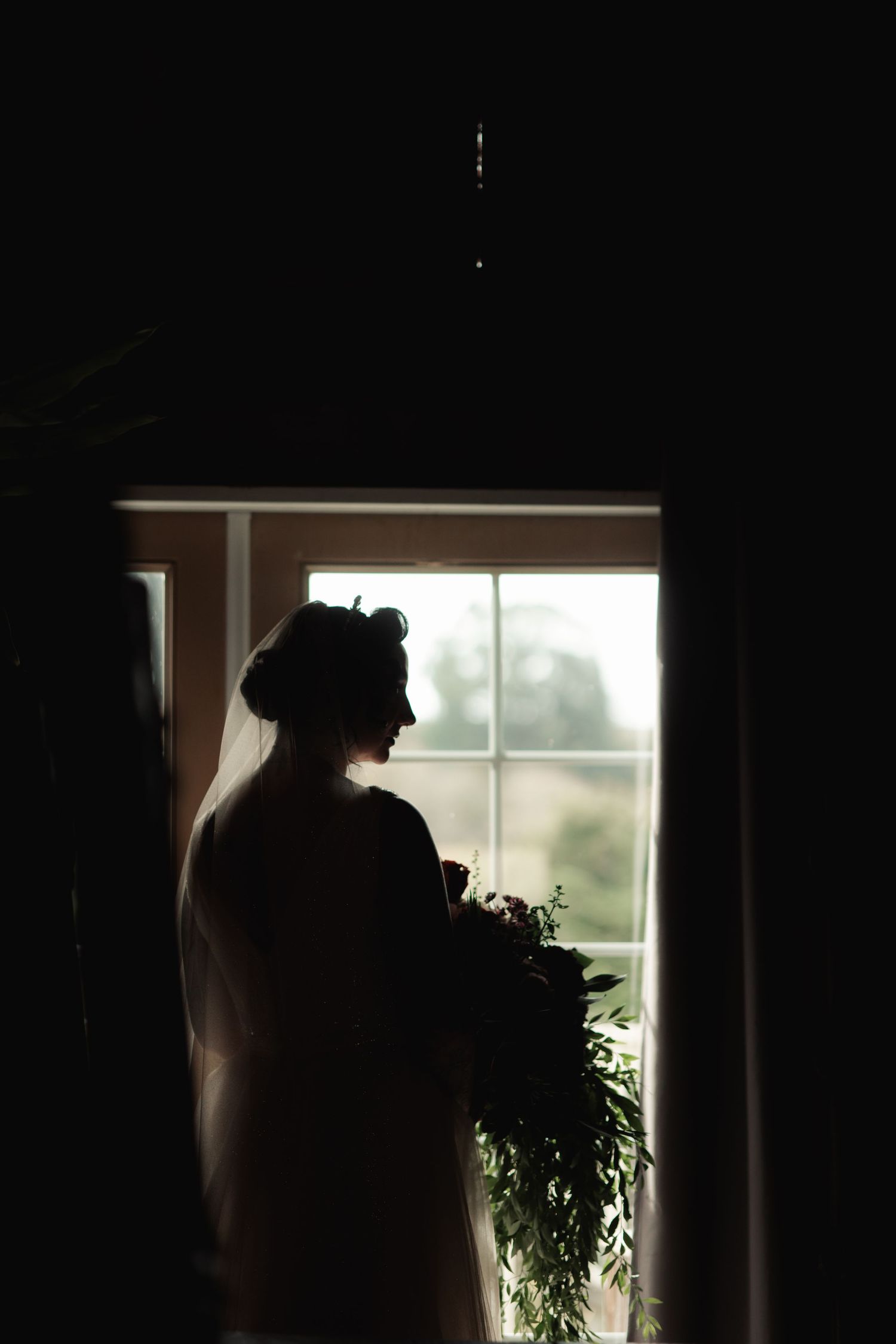 Silhouette of bride against bright window creating dramatic contrast.