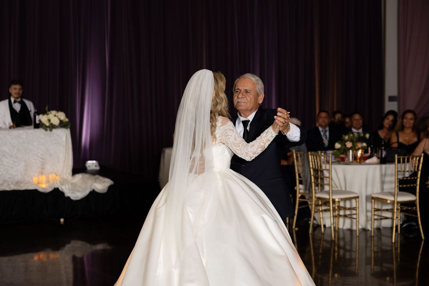 Wedding couple embraces on the dance floor surrounded by guests at an elegant reception venue.