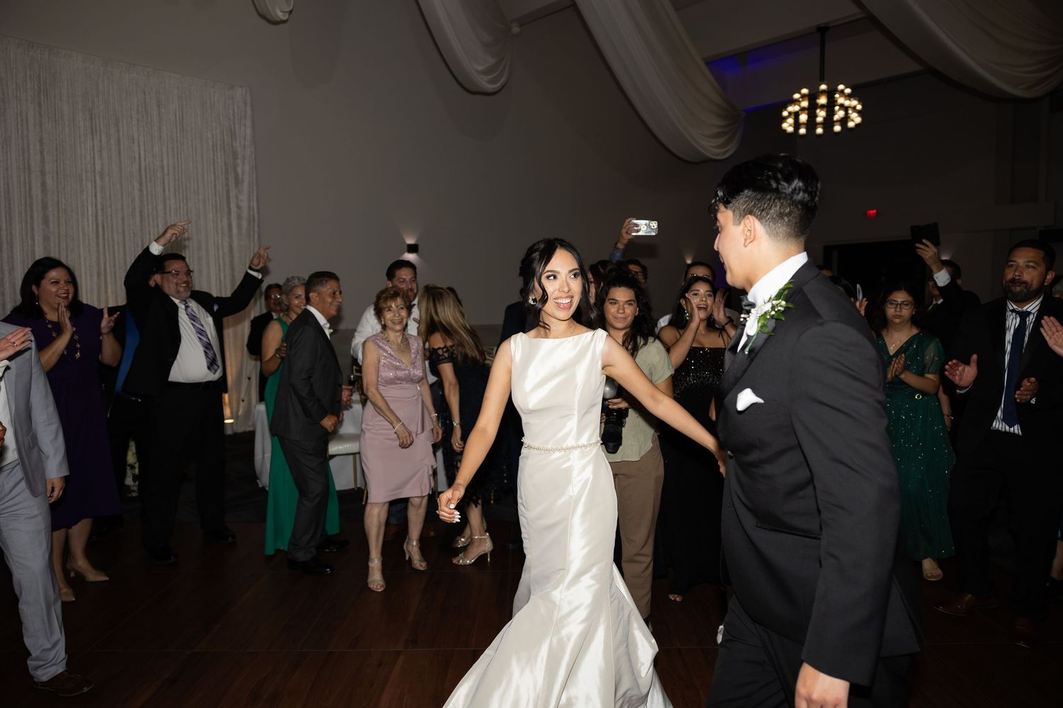 Wedding reception guests dancing together on a dimly lit dance floor with festive lighting.