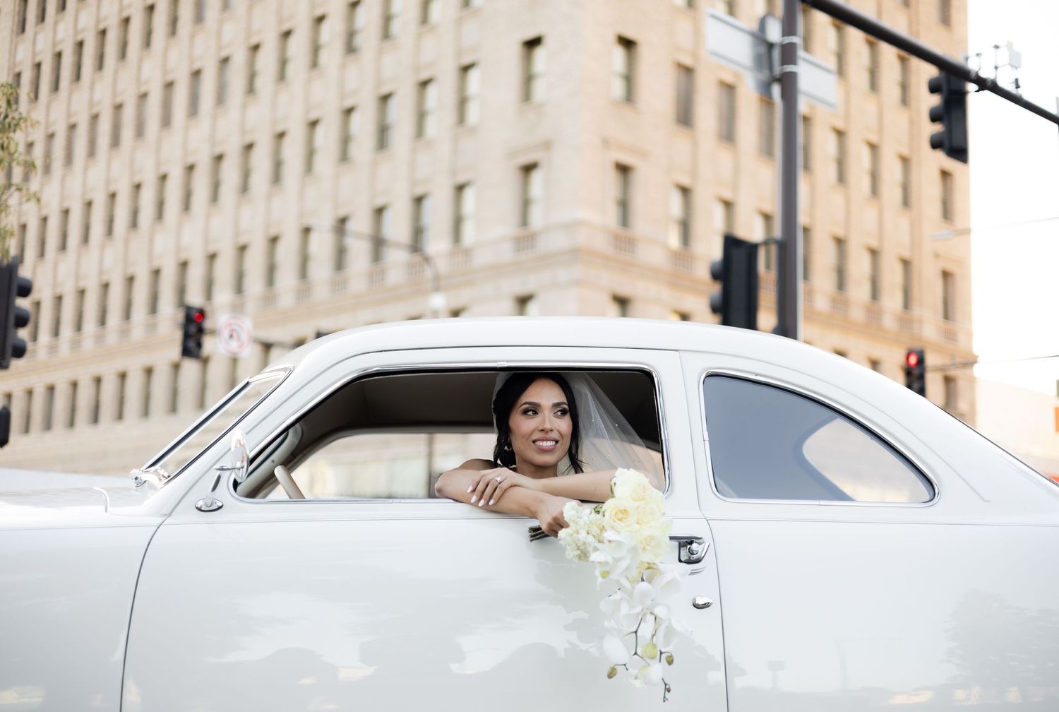 Classic white car with wedding decorations parked in front of stone building facade.