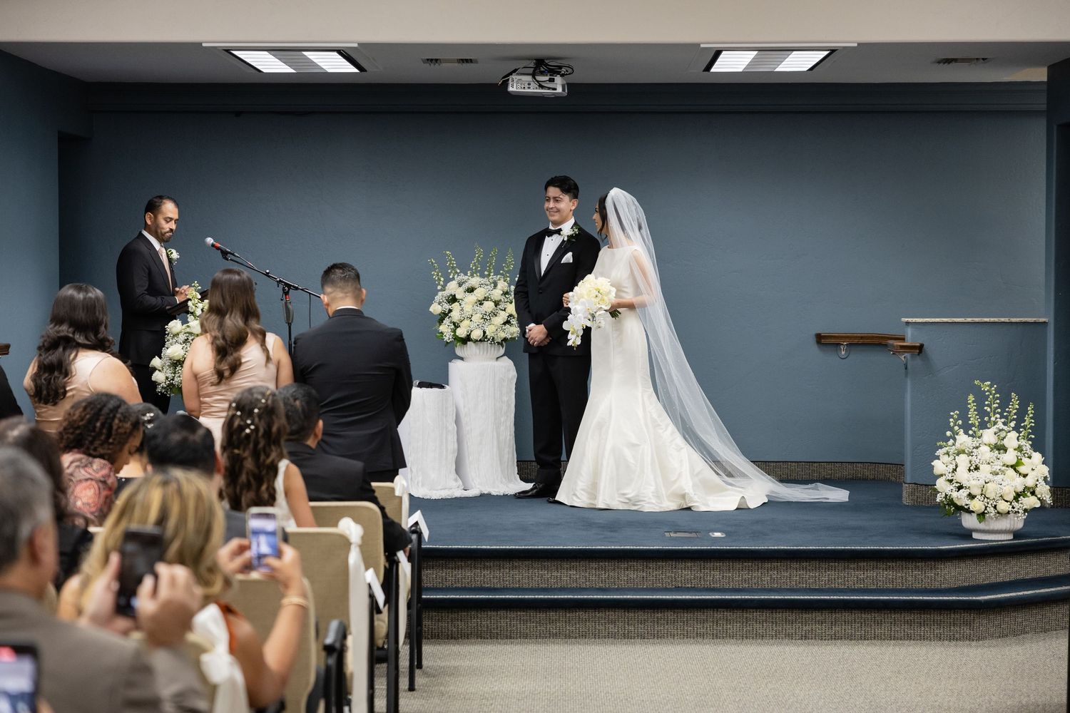 Wedding ceremony setup in a room with dark blue walls and white floral arrangements.