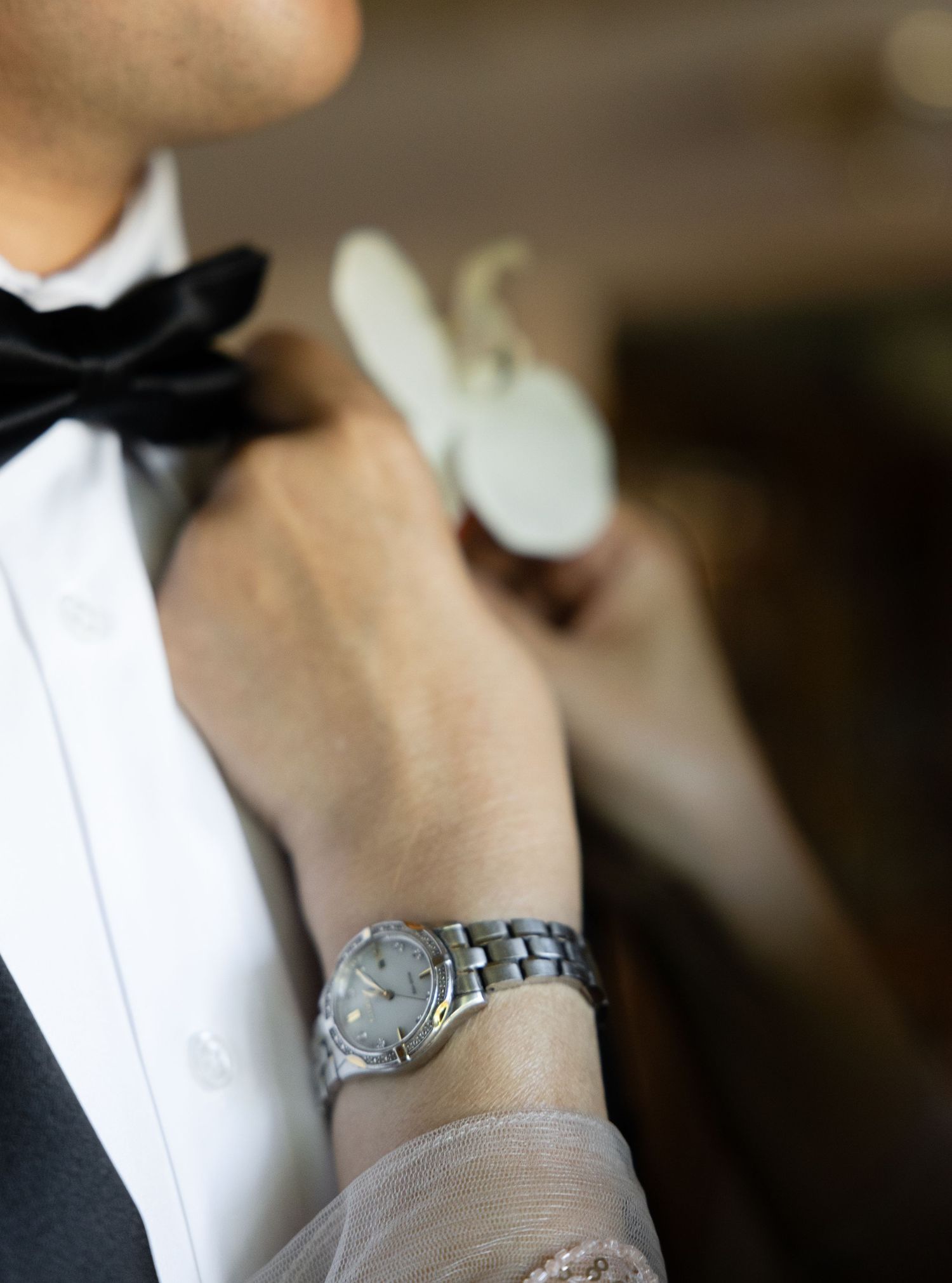 Close-up detail of a silver watch being worn with formal attire and black bow tie.