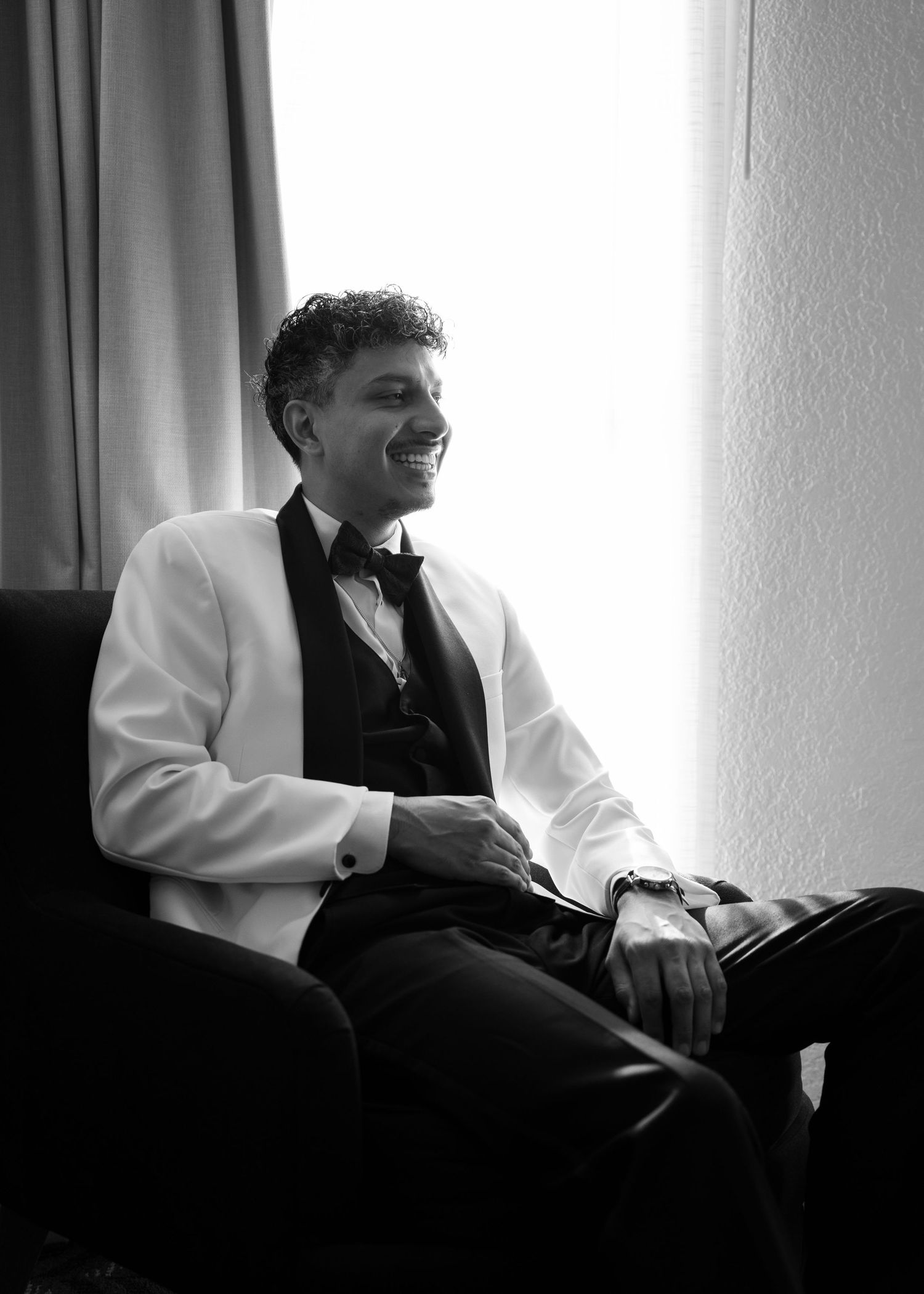 Black and white photo showing relaxed moments in formal attire by a window.