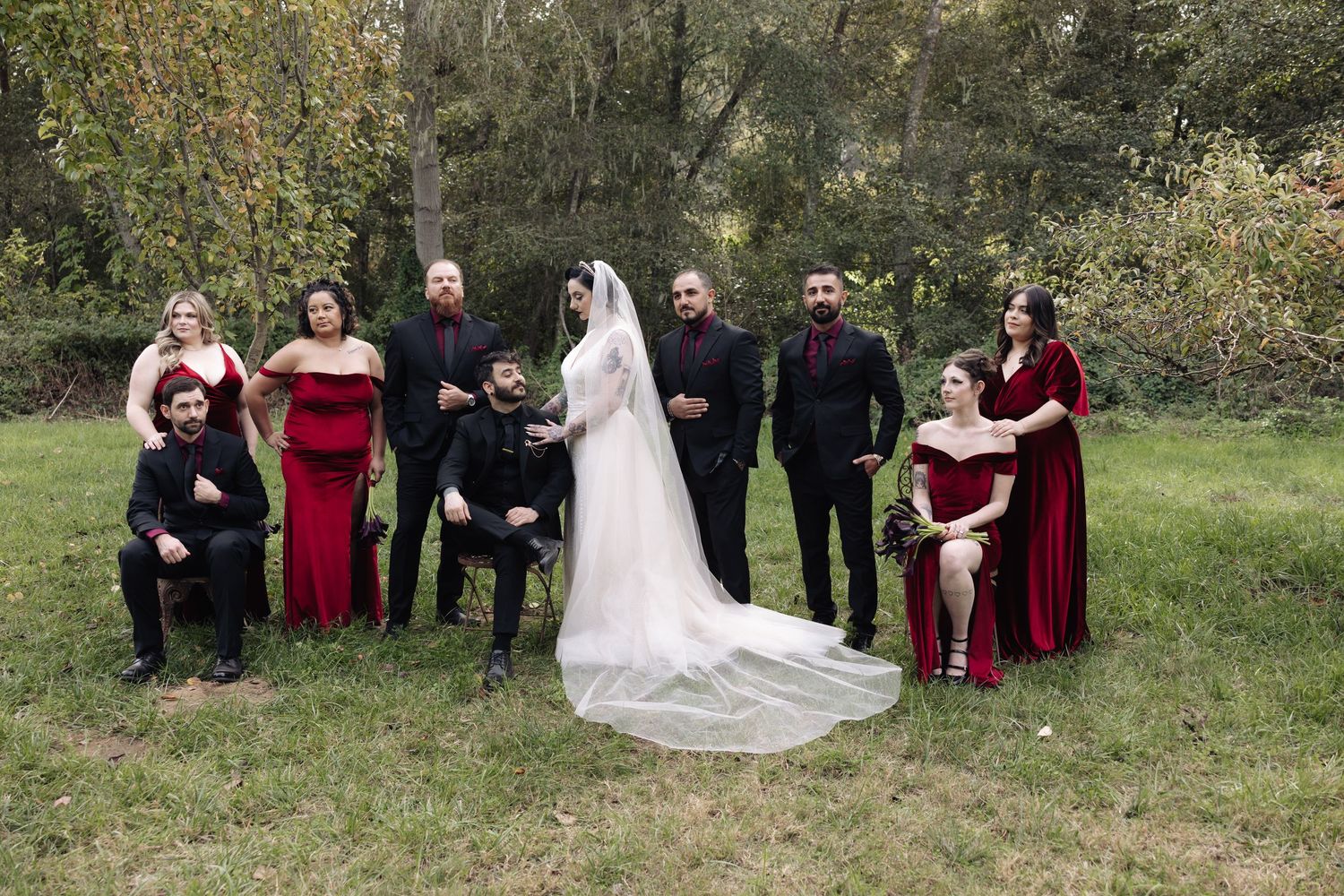 Outdoor wedding group photo with burgundy bridesmaids dresses against natural foliage.