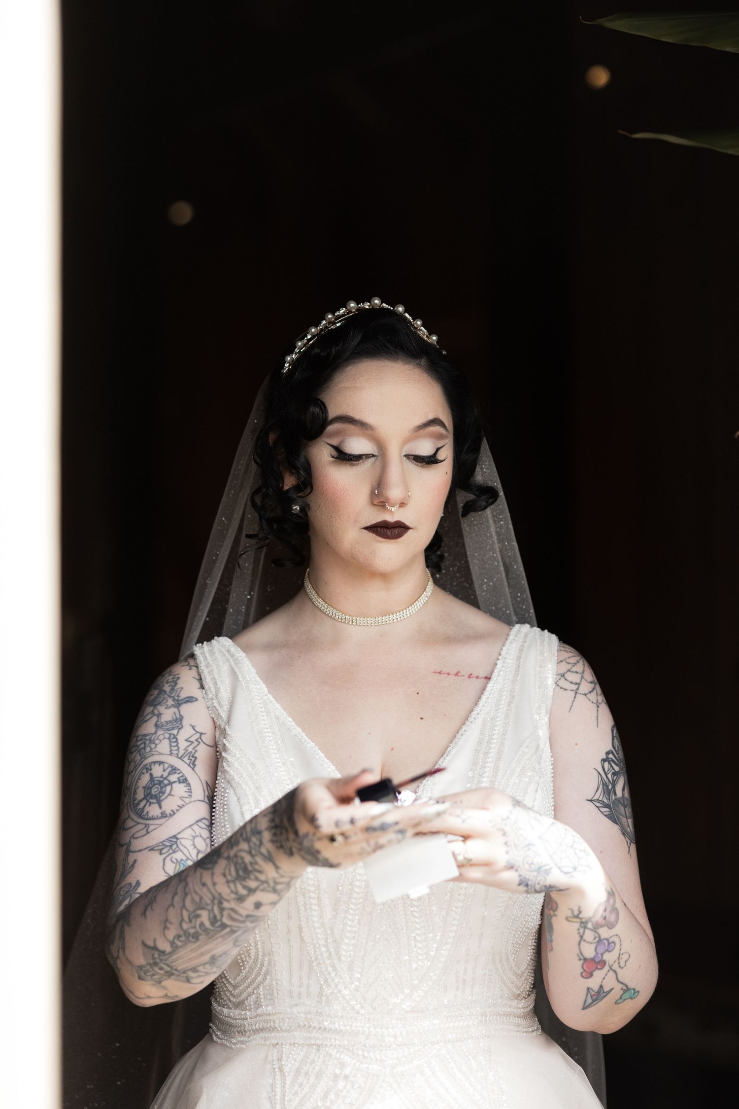 Bride in white dress with visible tattoos looking down at something in her hands.