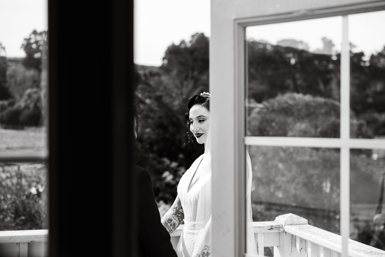 Black and white portrait of bride looking over shoulder through window frame.