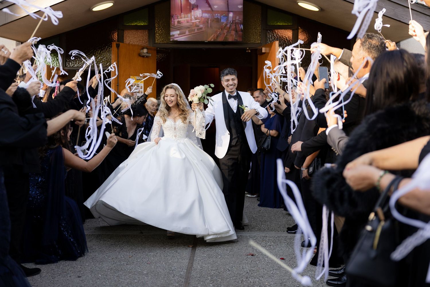 Newlyweds exit church under shower of white ribbons from celebrating guests.