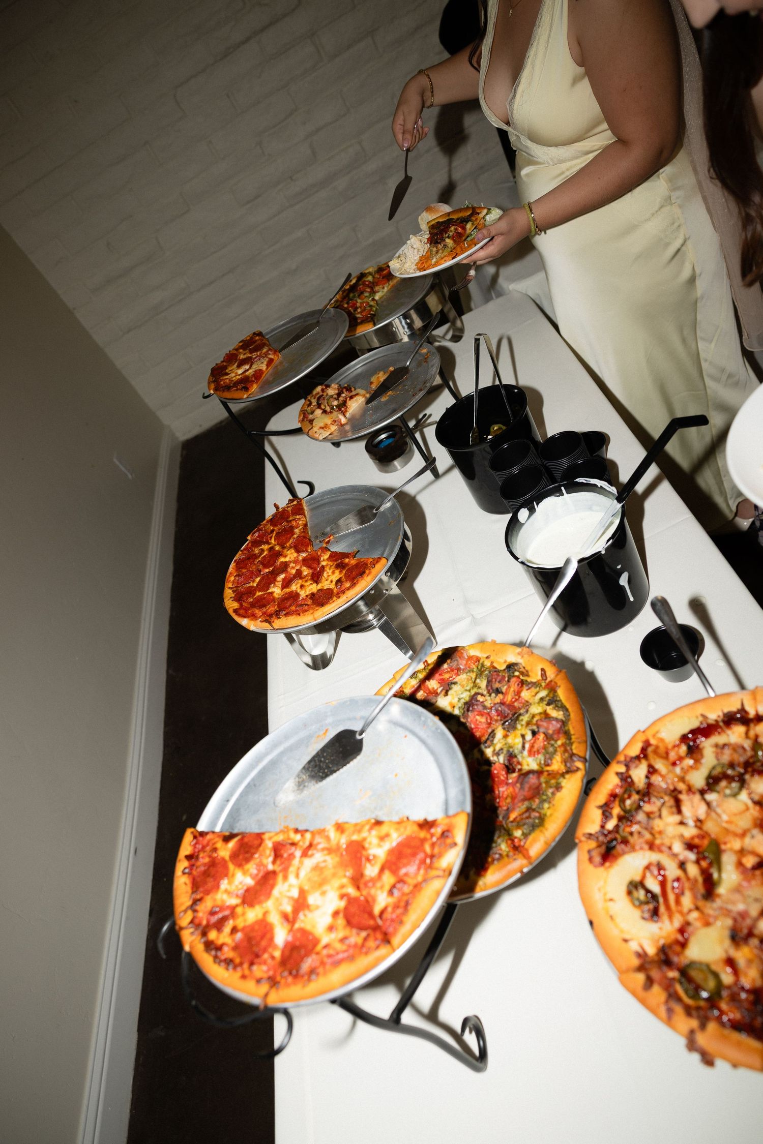 Wedding reception pizza buffet with variety of toppings on elevated stands.