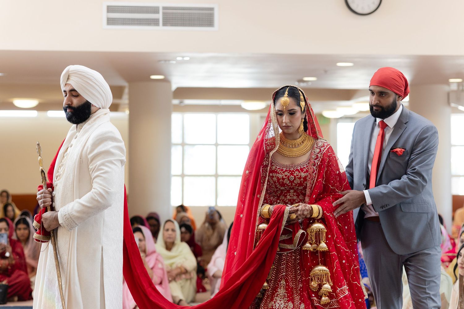 A traditional Sikh wedding ceremony with the couple in red and gray attire seated during the religious rituals.