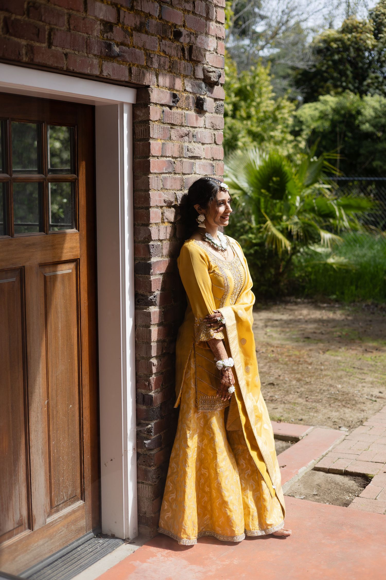 Yellow traditional dress against rustic brick wall and wooden door in natural sunlight.