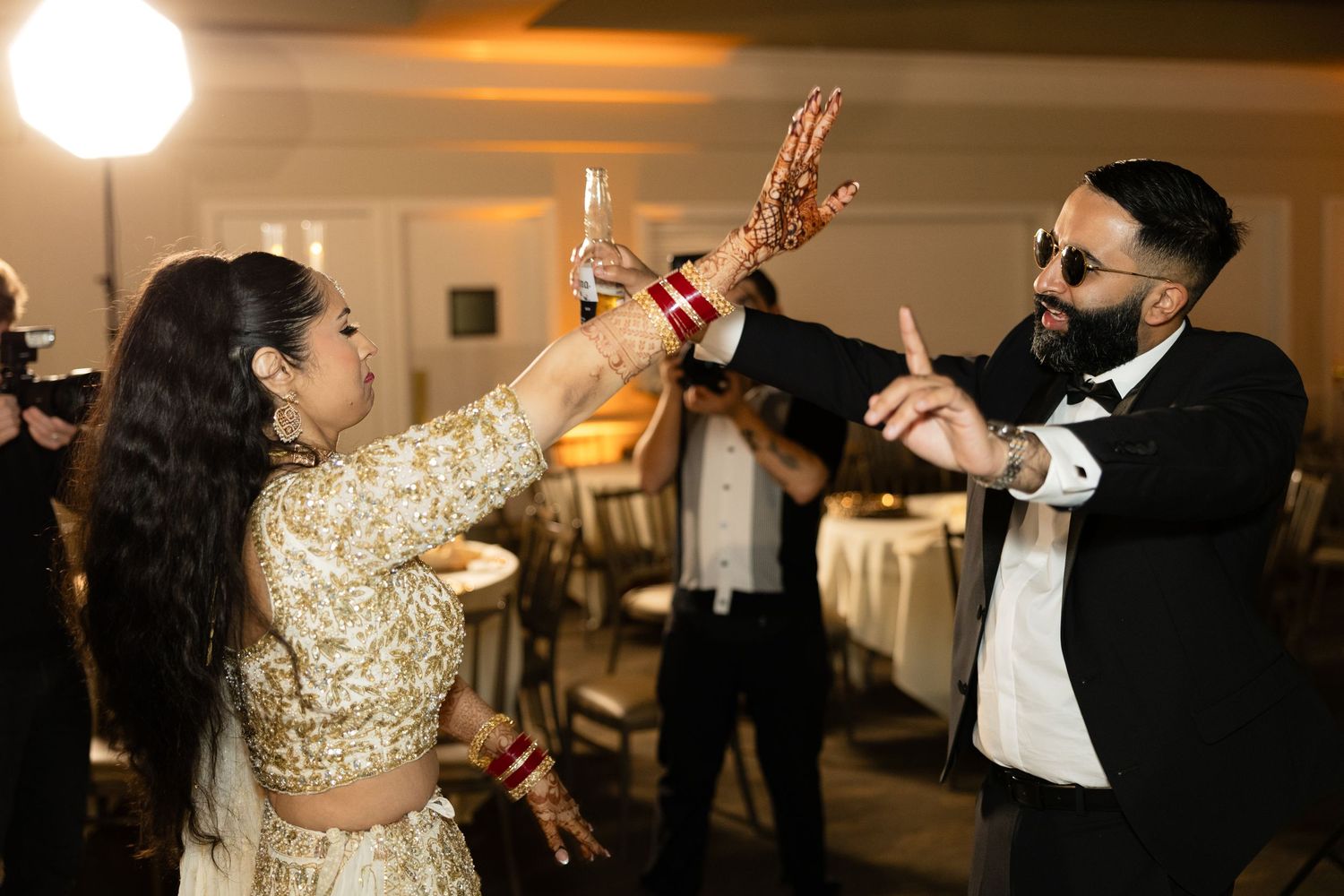 Two people dance energetically at a wedding reception in formal attire with gold and white decor.