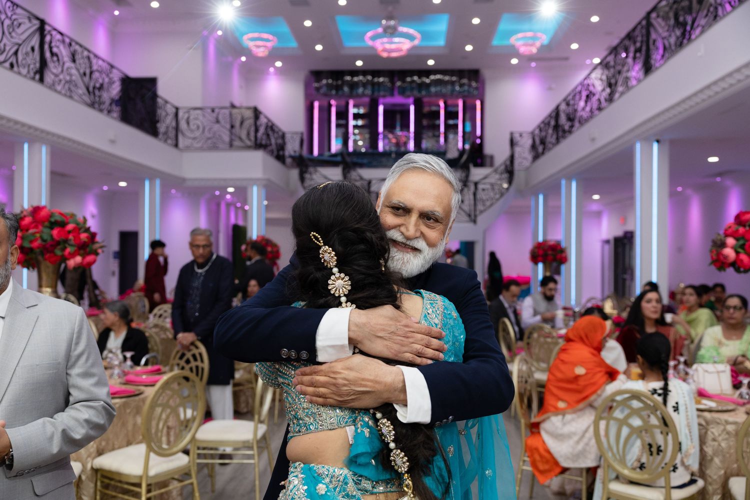 Guests enjoying a festive celebration in an elegant banquet hall with purple lighting and decorative floral arrangements.