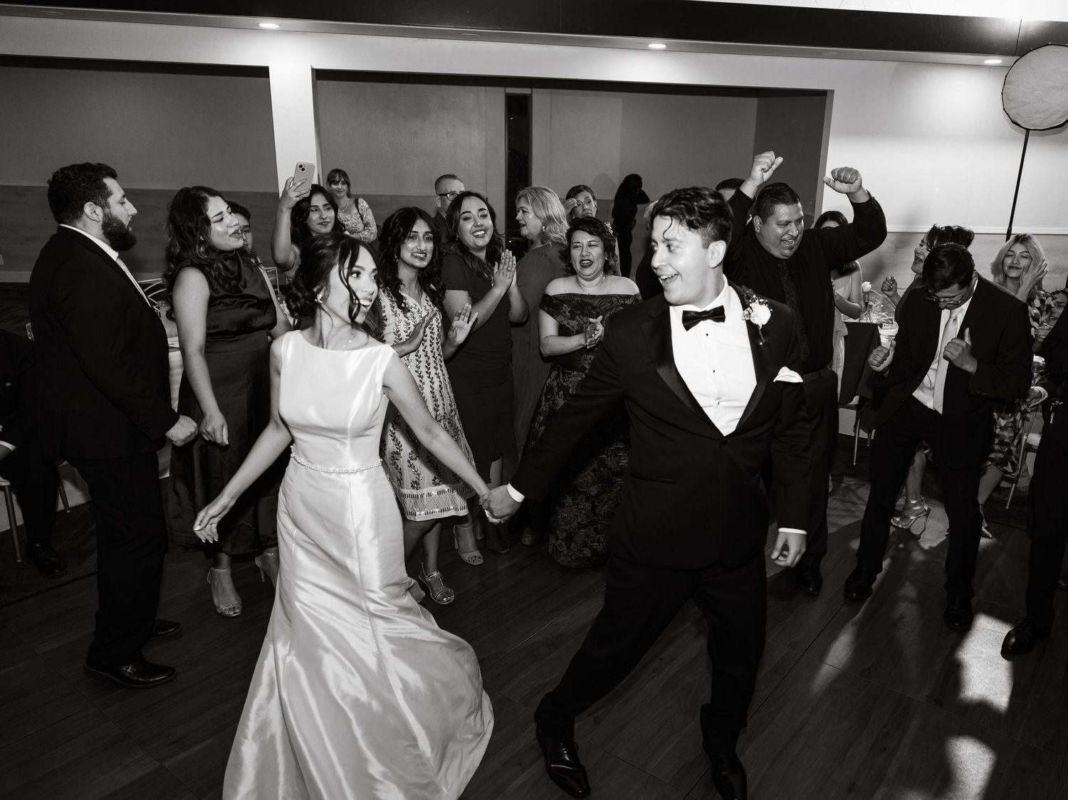 Bride in white dress dancing with wedding guests during reception celebration.