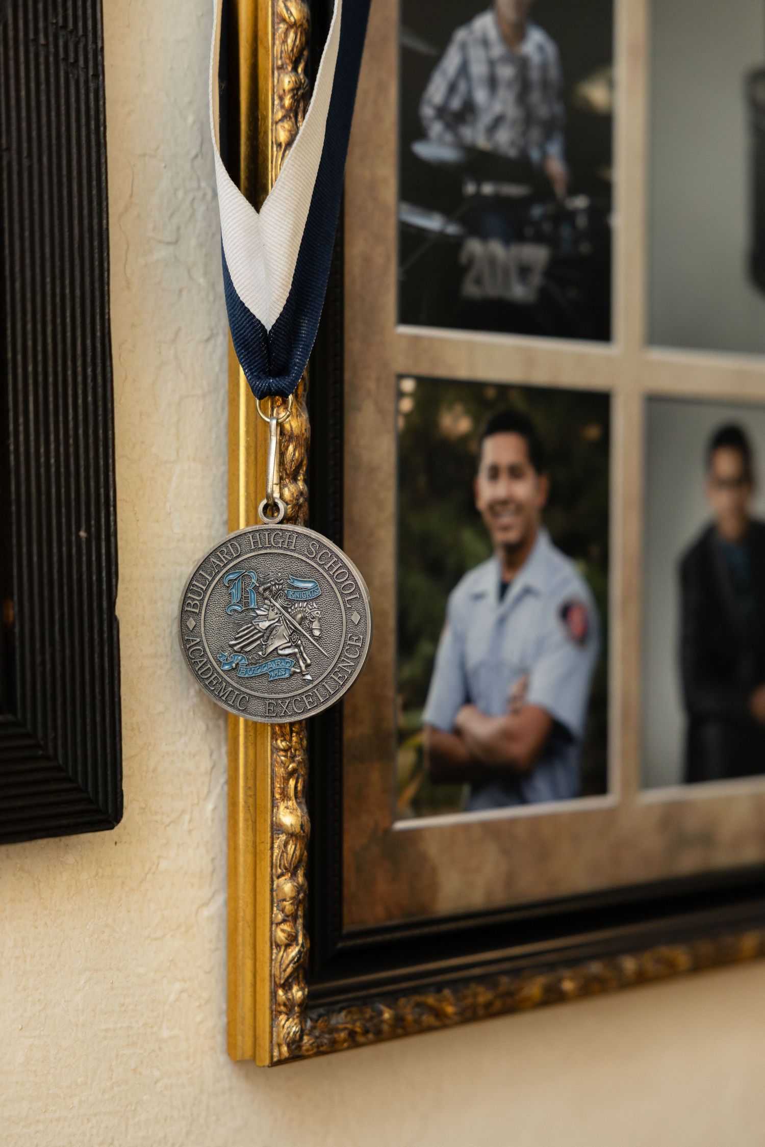 Framed medals and awards displayed on a wall with gold trim and photographs.