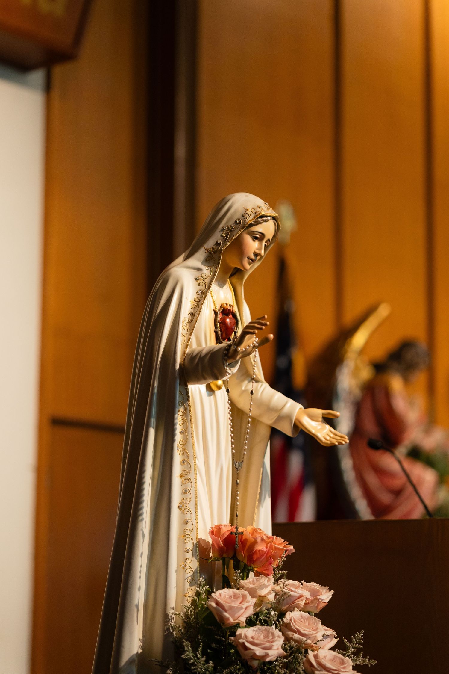 Religious statue of Mary adorned with pink roses in a church setting.