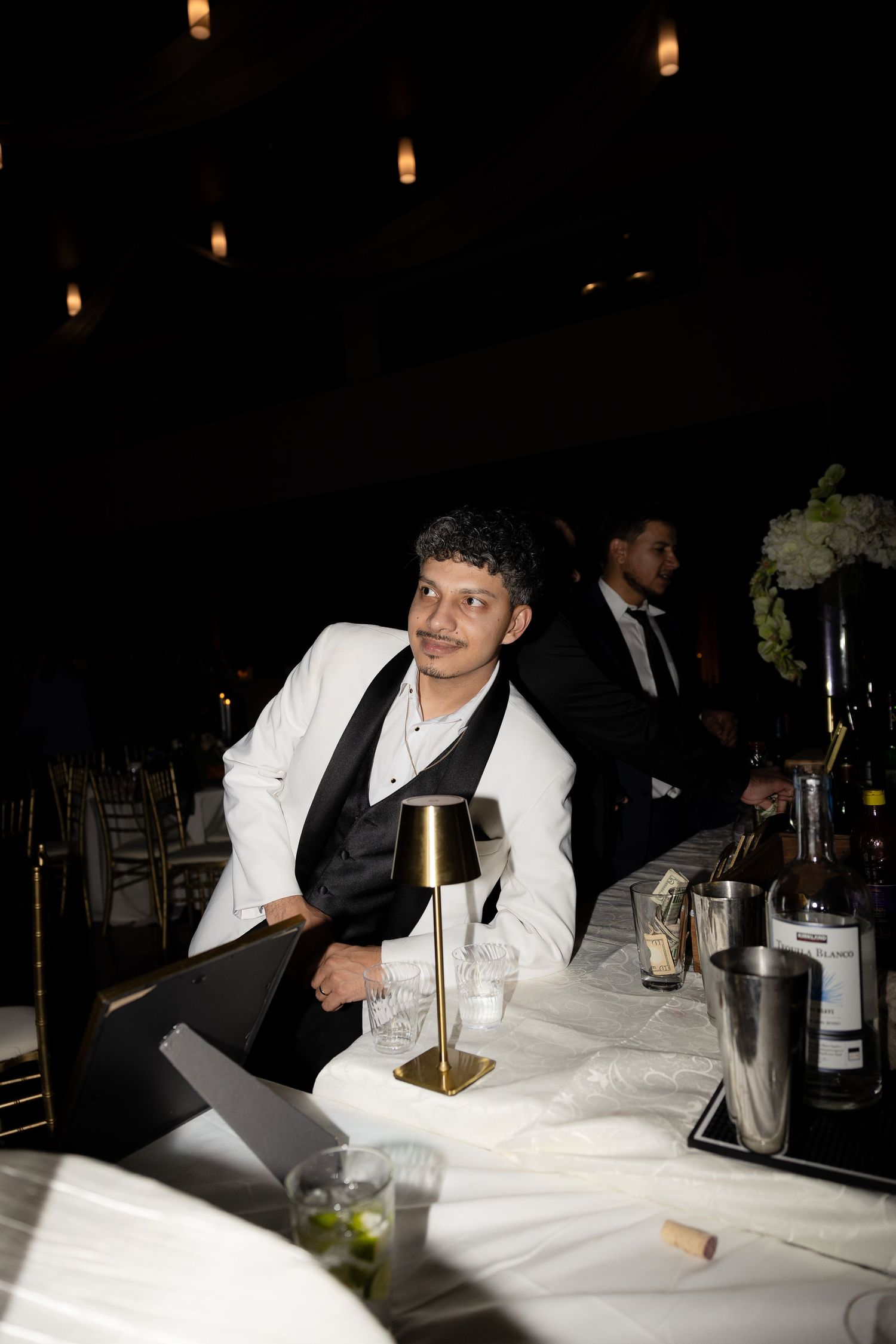 Wedding guests seated at tables with white tablecloths in dark reception venue.