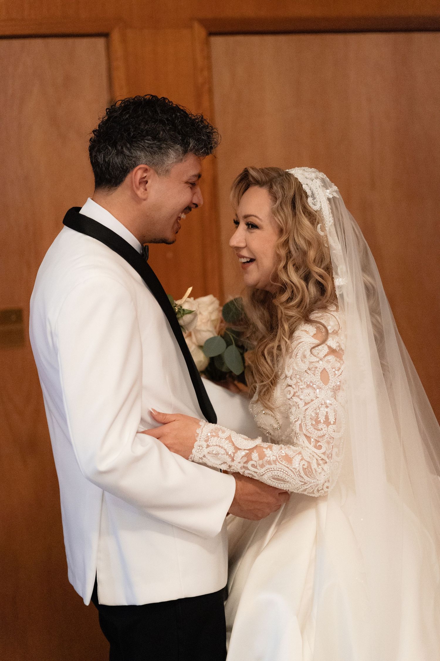 Joyful moment between newlyweds in white attire during their wedding day.
