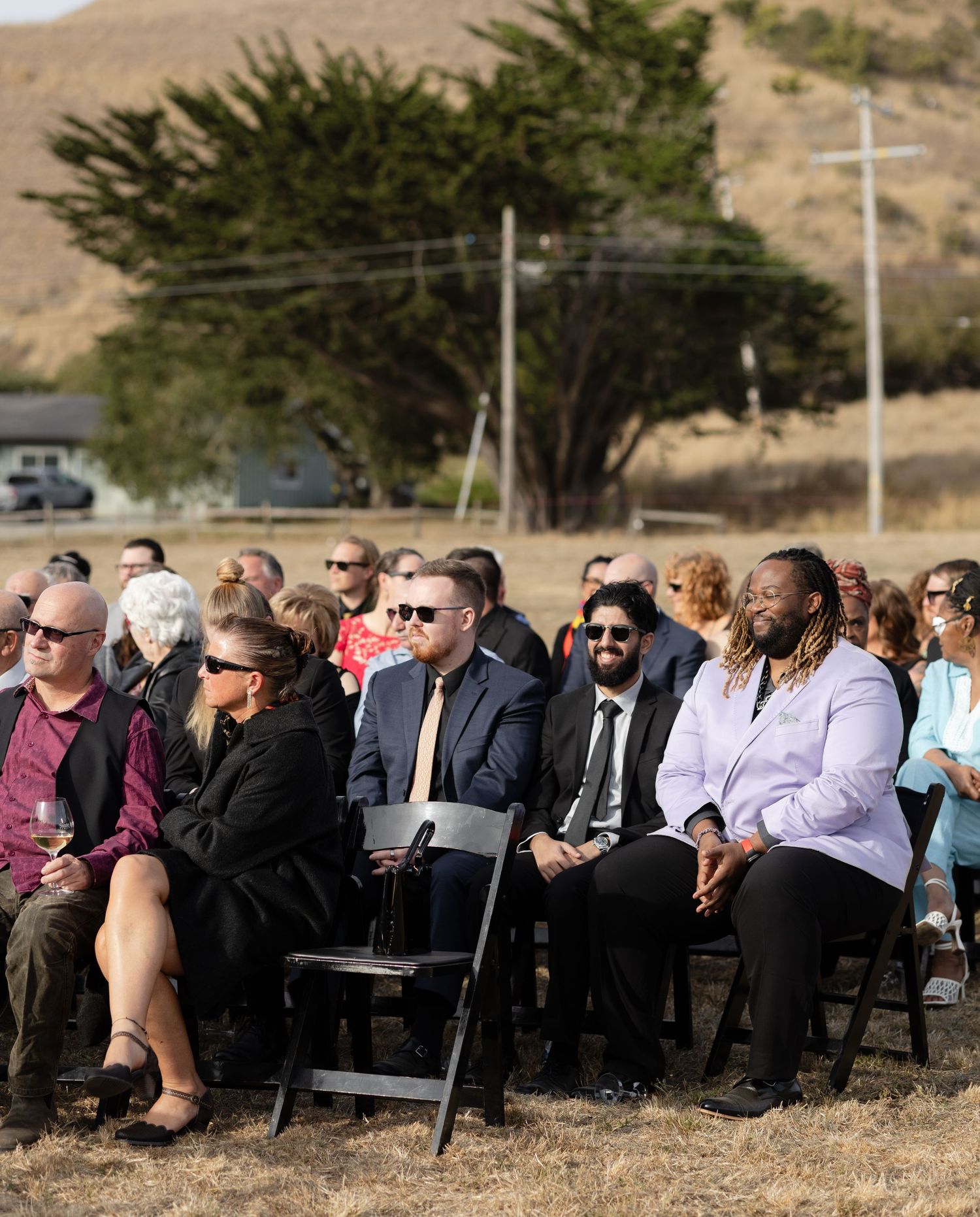 Wedding guests seated in rows of black chairs at an outdoor ceremony.