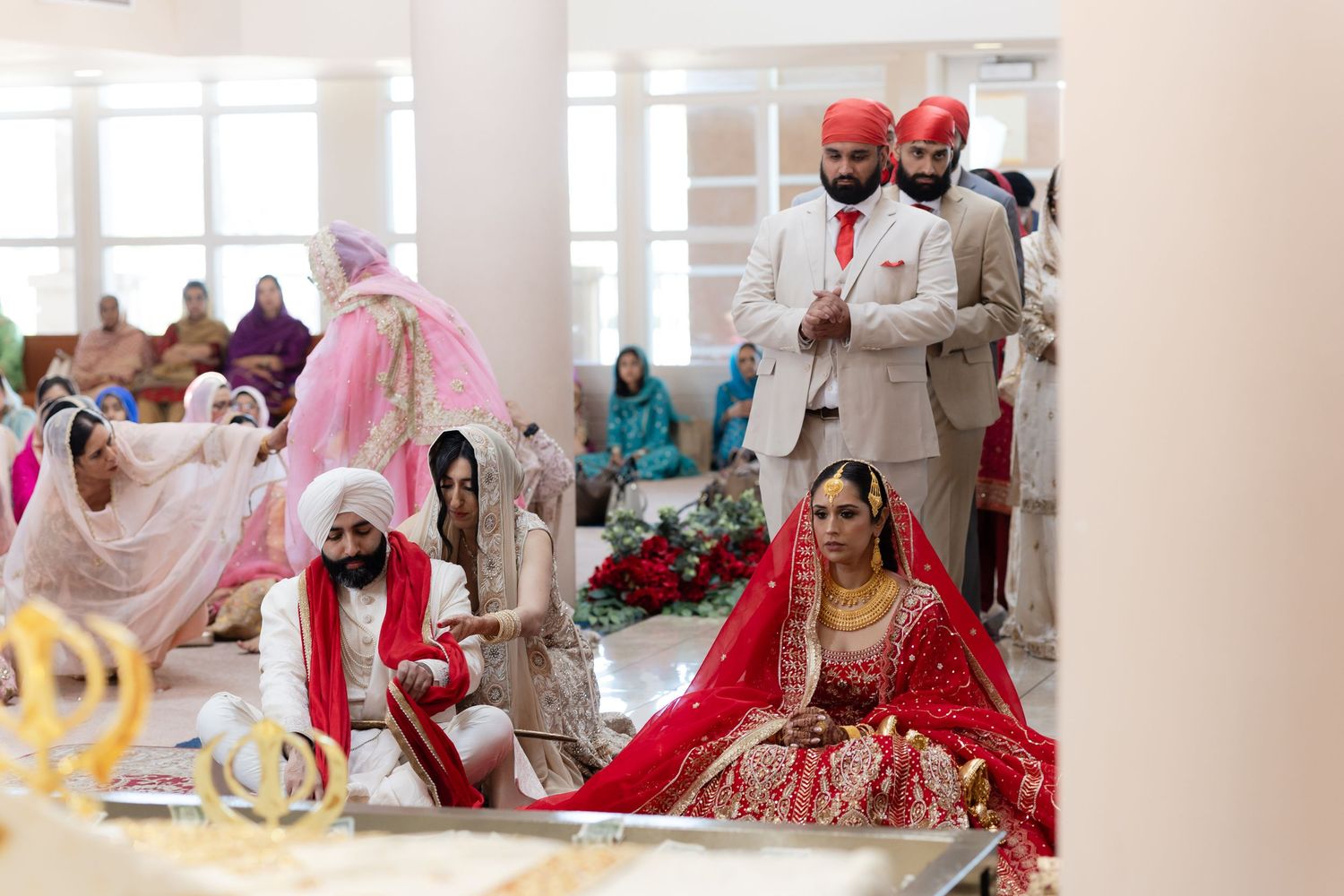 A traditional South Asian wedding ceremony with guests in vibrant red and white attire seated in an elegant venue.