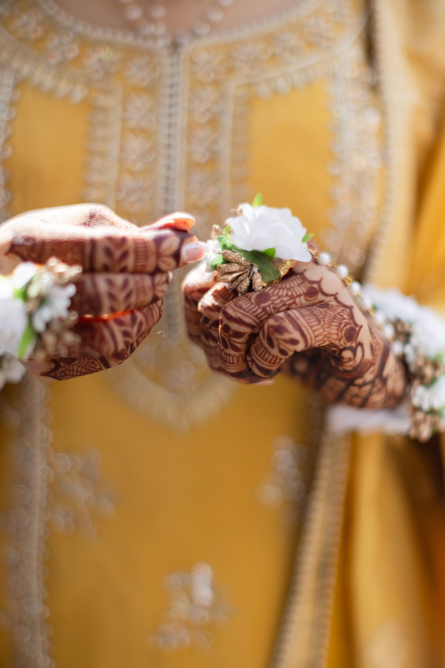 Close-up detail of intricate henna designs on hands with white flowers against a golden background.