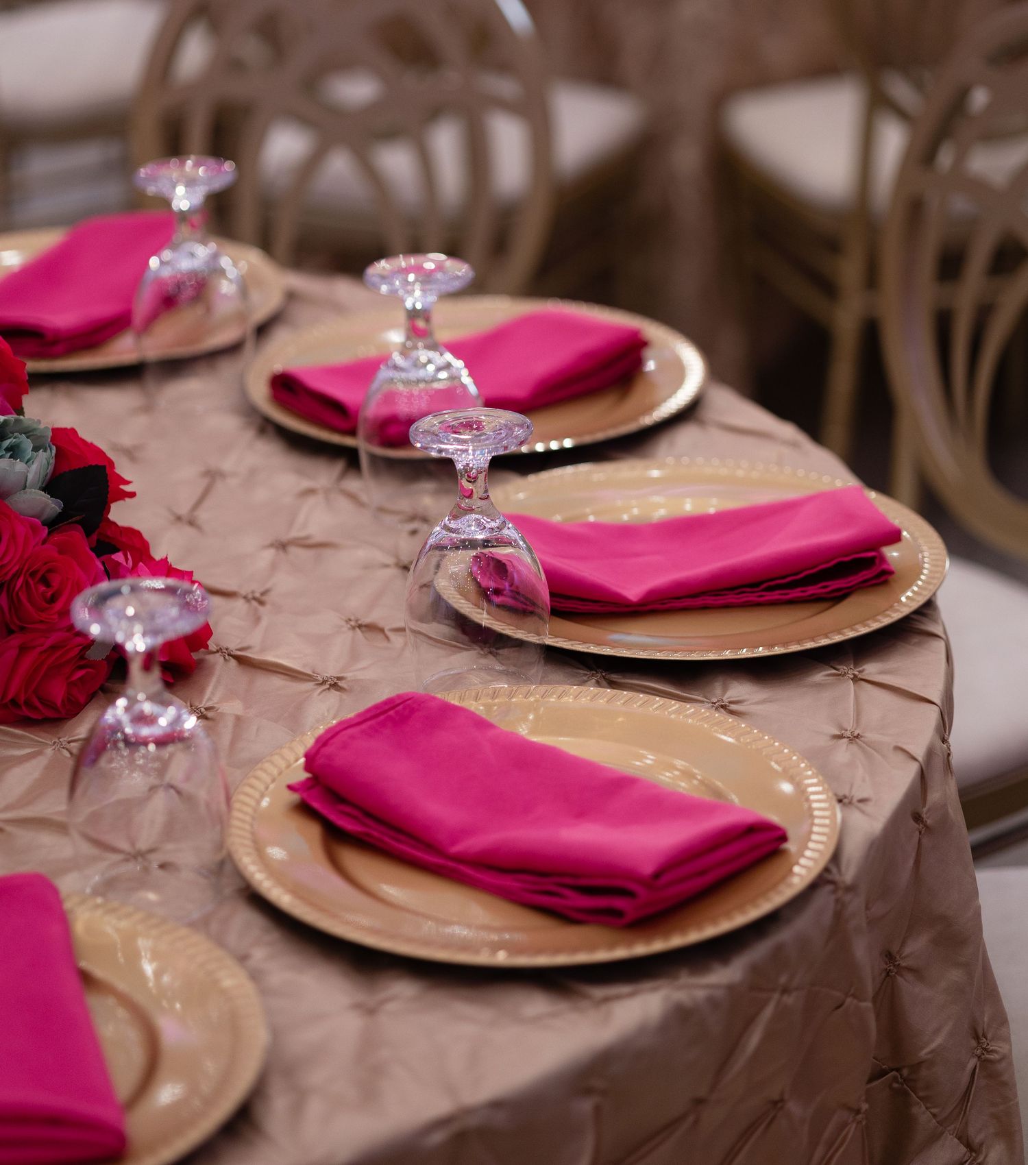 Elegant table setting with gold charger plates, pink napkins, and crystal stemware on a brown tablecloth.