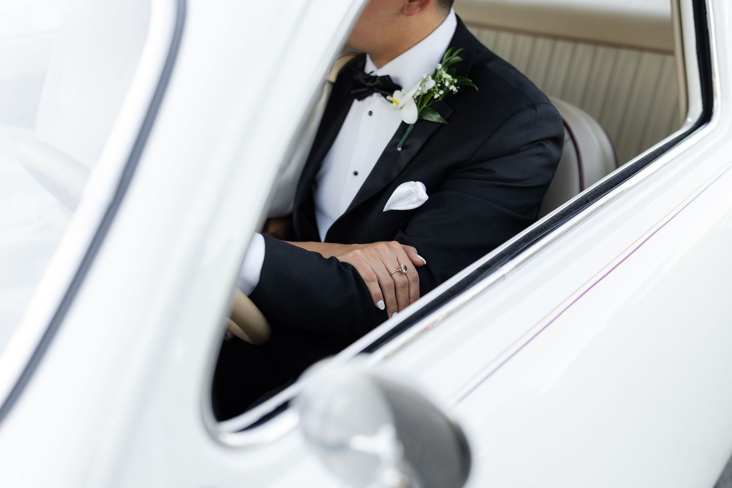 Wedding couple sits close together in a classic white automobile.
