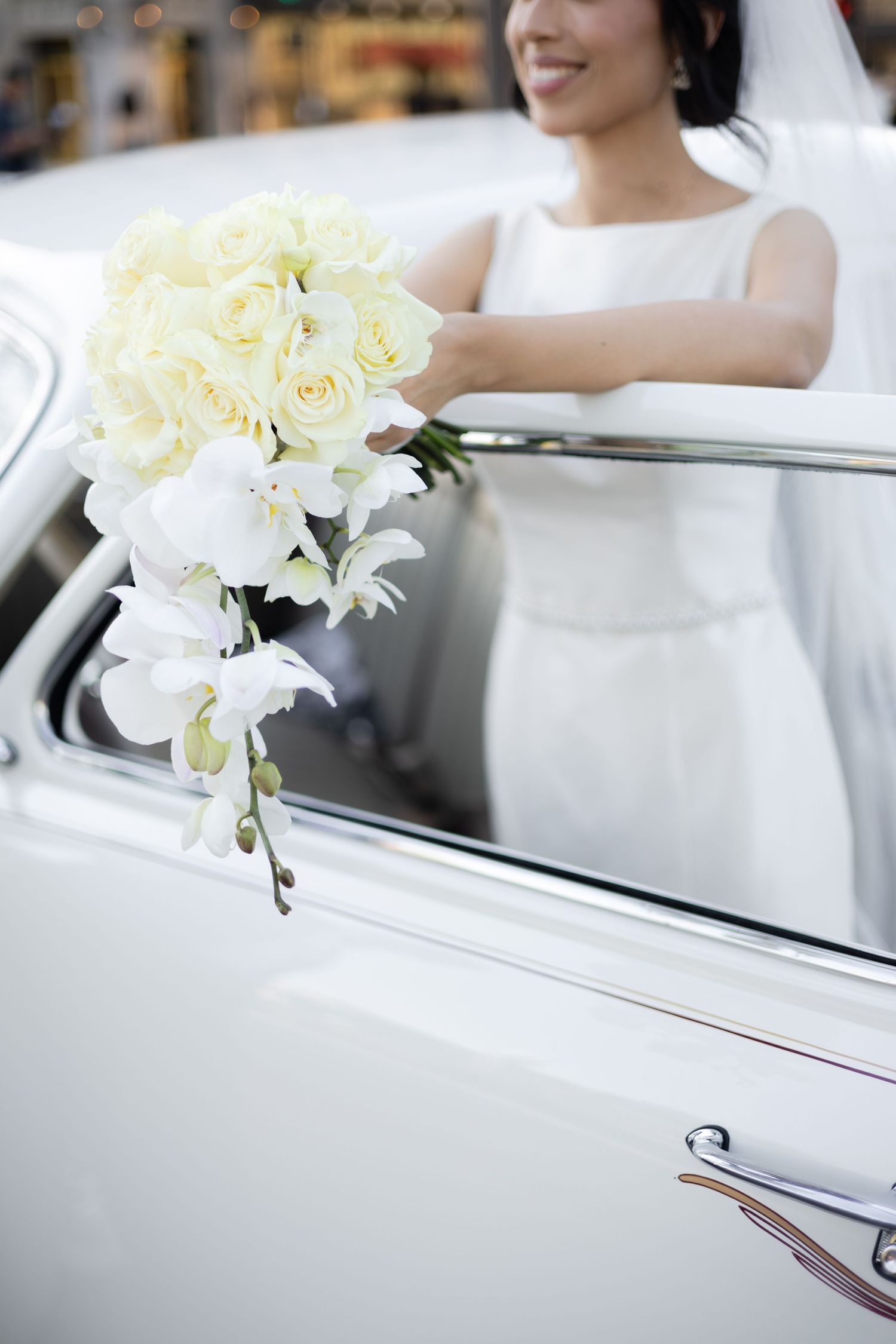 White roses and orchids decorate vintage car door for elegant wedding transportation.