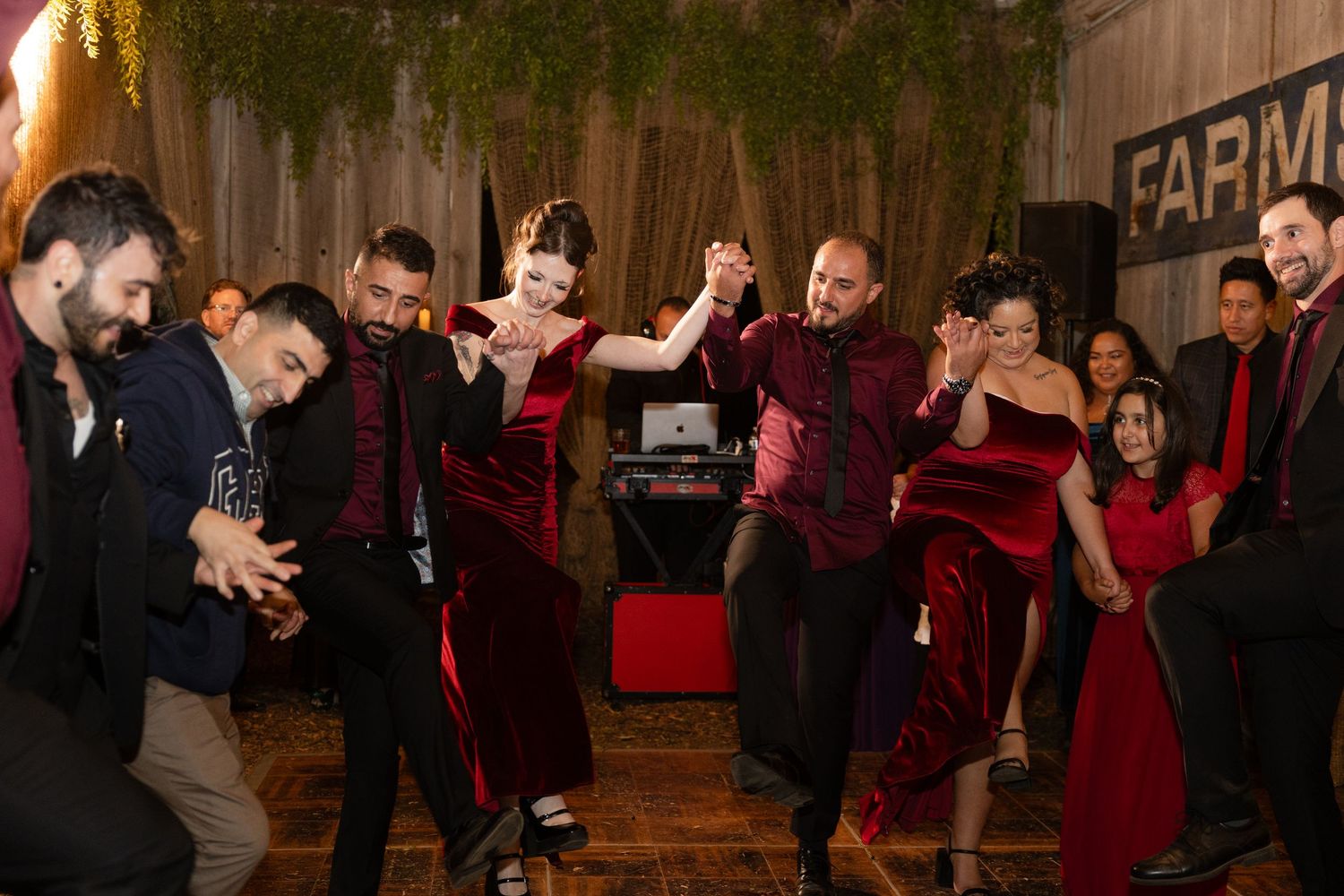 Wedding guests enjoying themselves on a wooden dance floor under warm lighting.