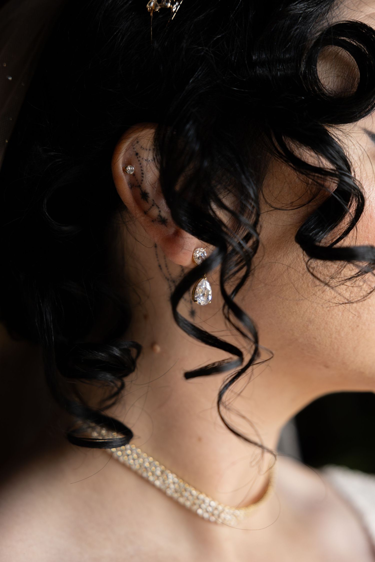Close-up detail of pearl jewelry and dark curled hair against soft lighting.