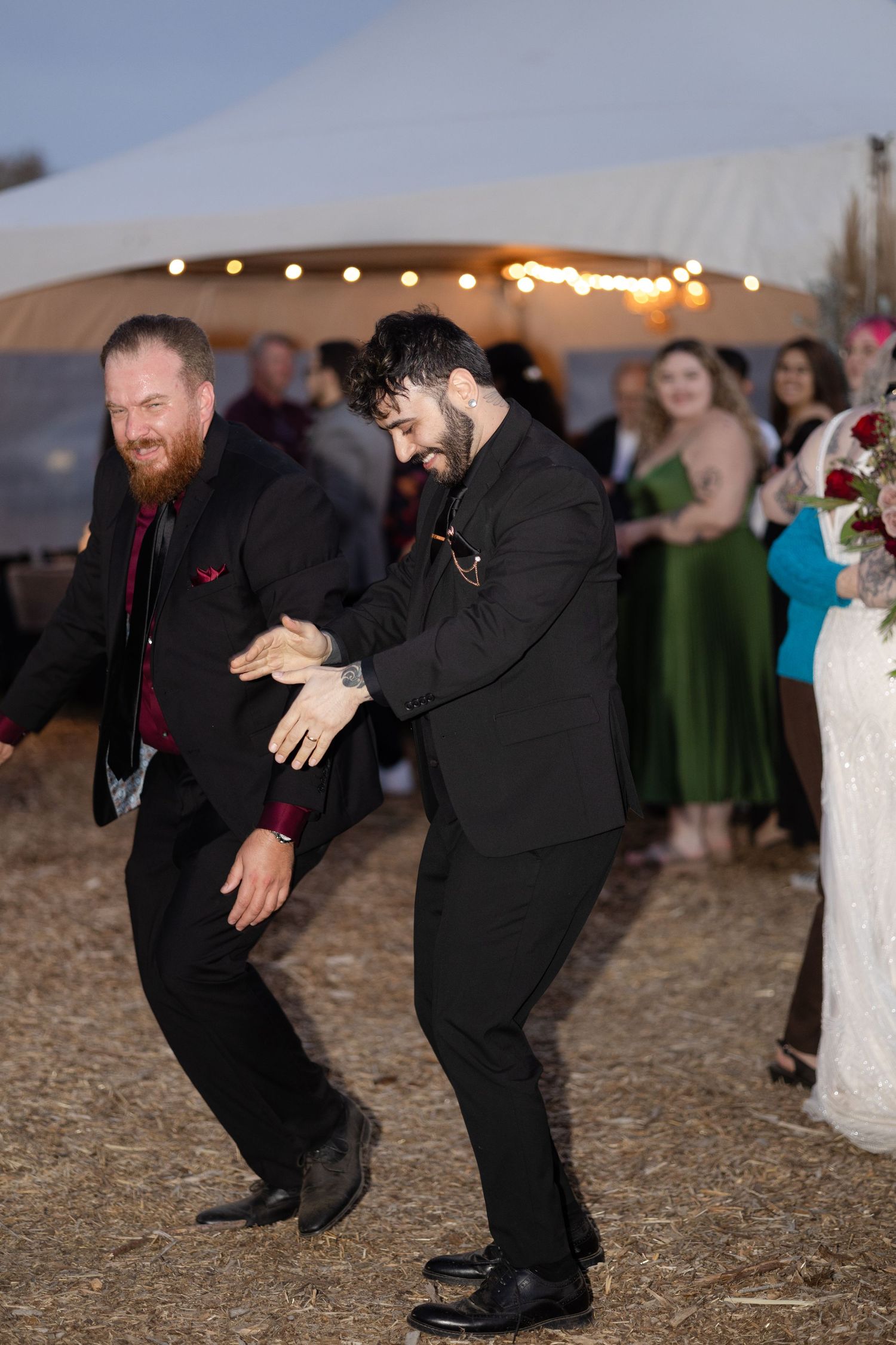 Wedding guests perform energetic dance moves on an outdoor dance floor.