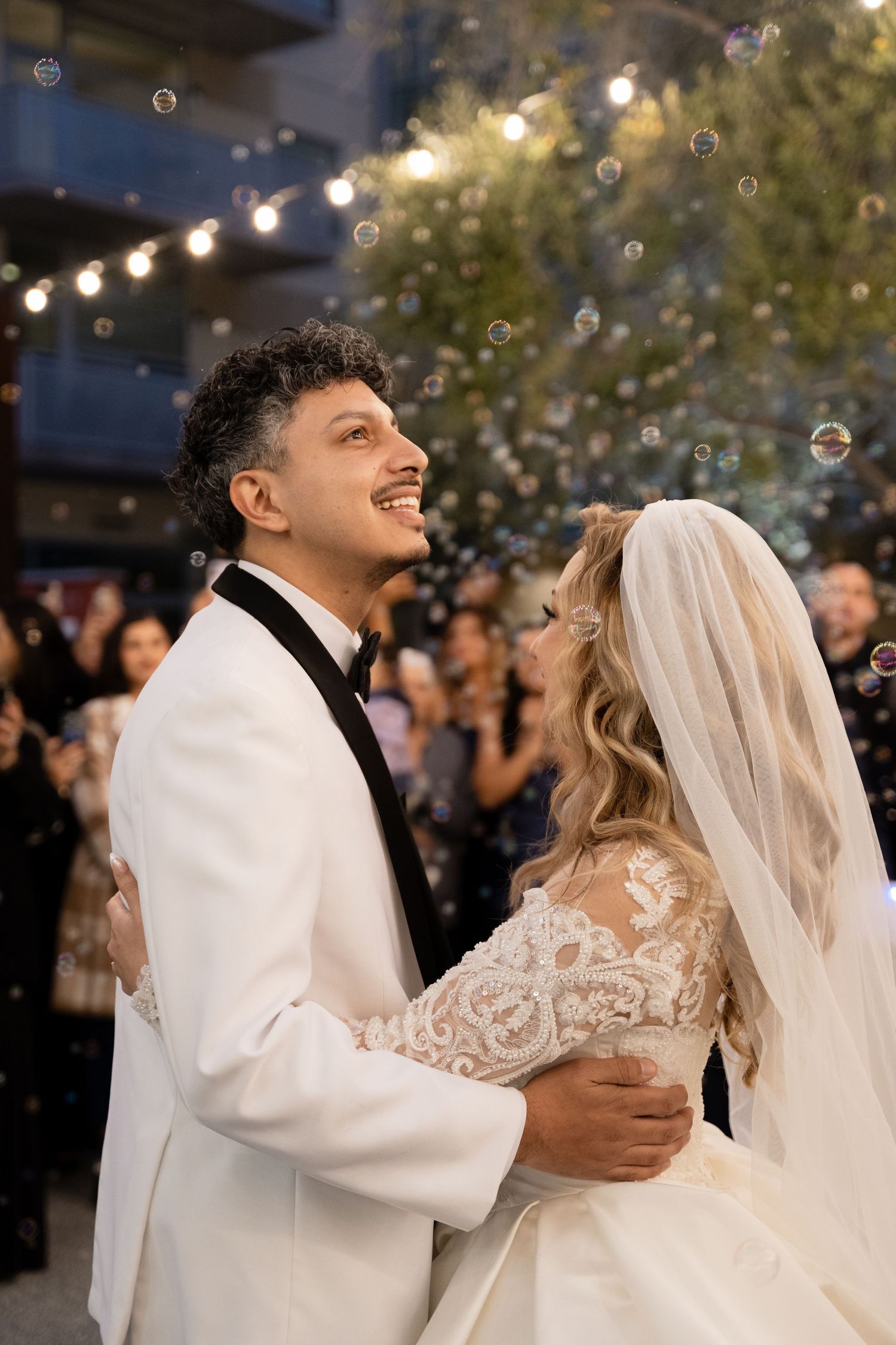 Joyful couple dances beneath string lights and bubbles during their wedding celebration.
