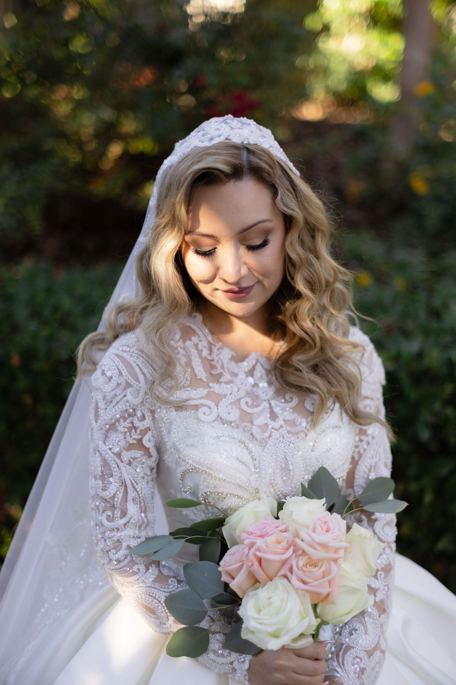 A close-up of a bride wearing a detailed lace wedding dress and holding a soft pink and white bouquet.