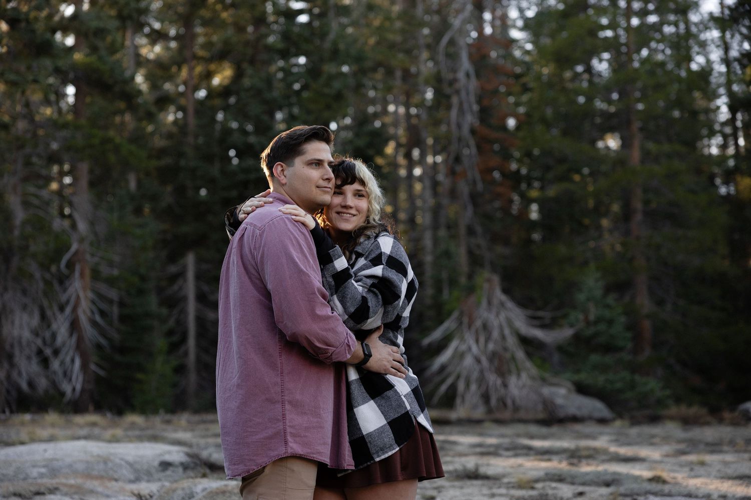 Couple embracing in a forest setting during golden hour photography session.