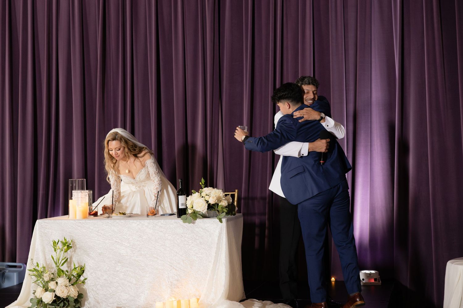 Candid reception moment captured at wedding head table with purple backdrop.