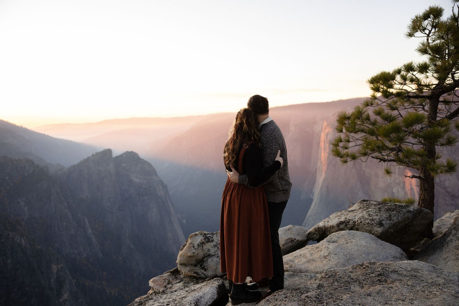 Two people share a romantic moment on rocky mountain terrain at dusk.