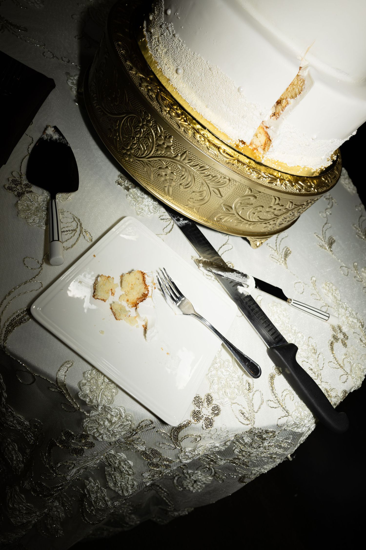 Closeup of a smashed white wedding cake on a table with scattered pieces and utensils.