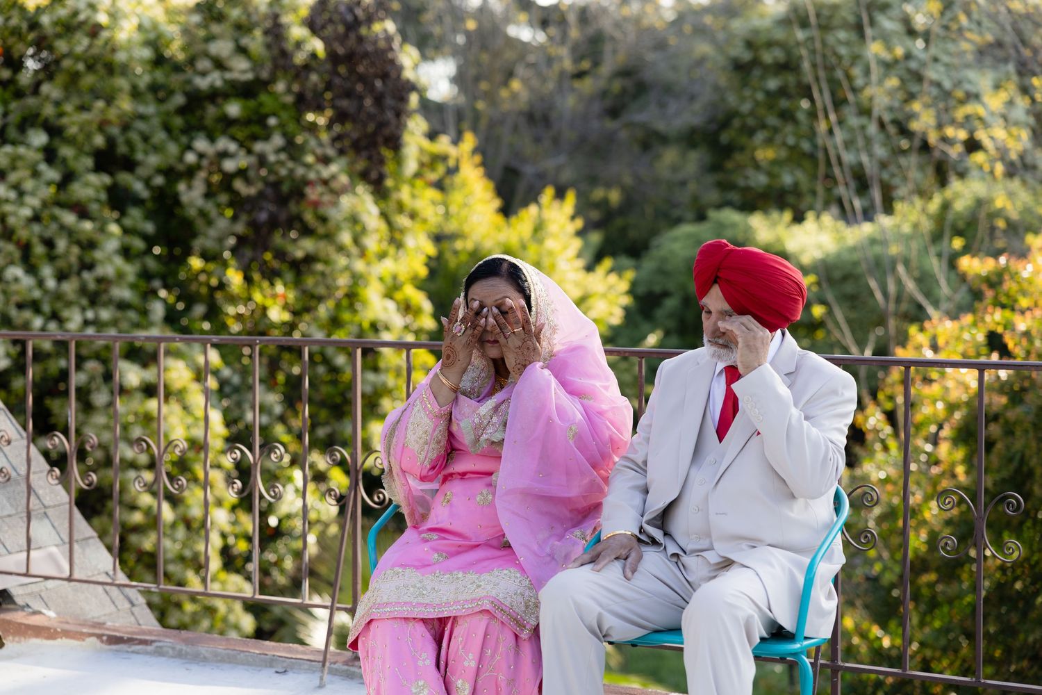 Couple in pink and white outfits sitting on bench in garden setting.