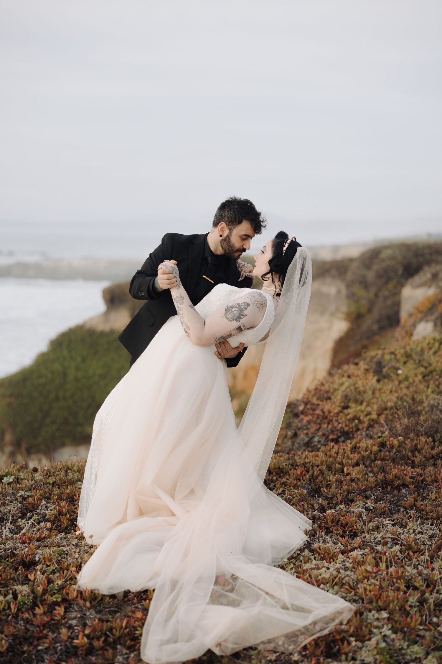 Romantic coastal wedding photos with flowing blush gown against dramatic cliffside backdrop.